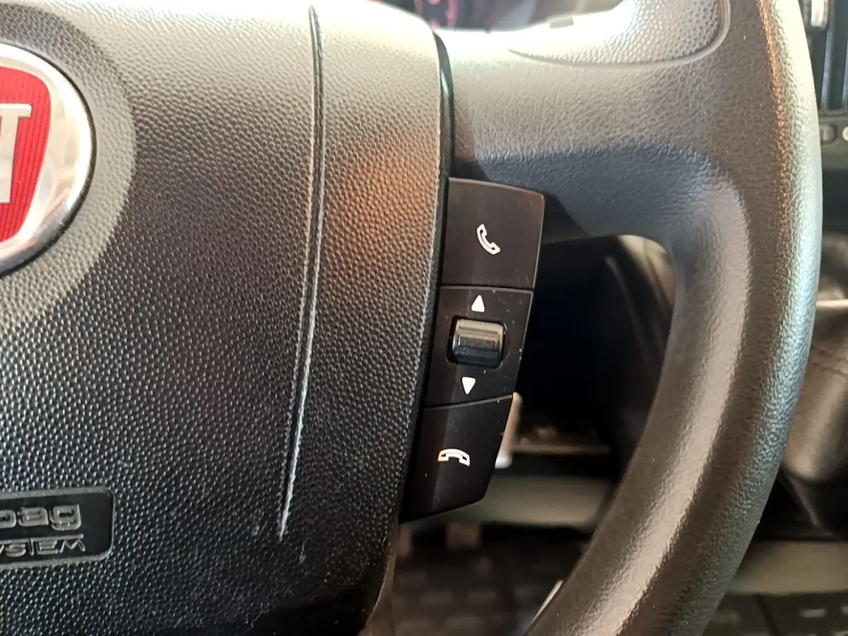Gros plan sur le volant noir multifonctions du Fiat Ducato Fourgon blanc, mettant en valeur les commandes d’appel téléphonique.