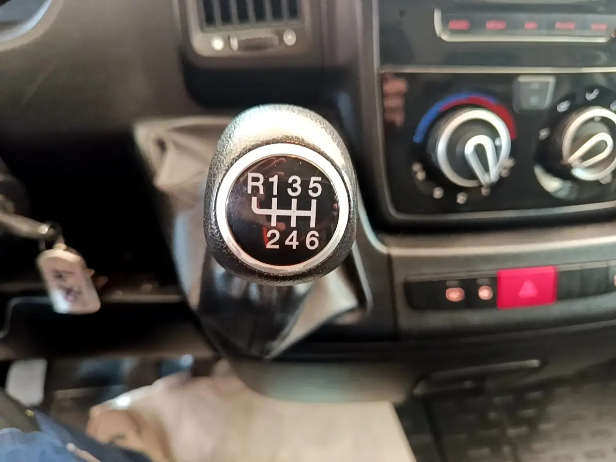 Gros plan sur le levier de vitesses manuel du Fiat Ducato Fourgon blanc, avec tableau de bord et commandes de climatisation en arrière-plan.