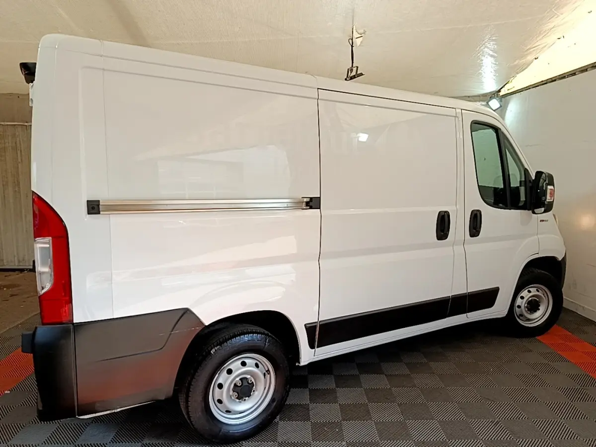 Fiat Ducato Fourgon blanc vu de profil côté droit, avec bande noire sur les bas de caisse et jantes acier.