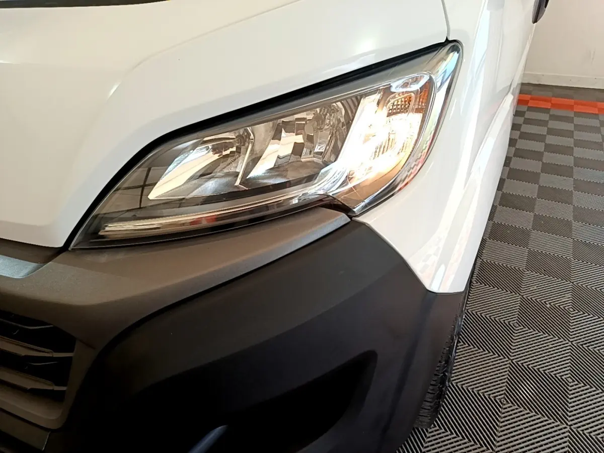 Gros plan sur le phare avant droit du FIAT Ducato Fourgon blanc, avec pare-chocs noir mat et partie de la calandre visible.