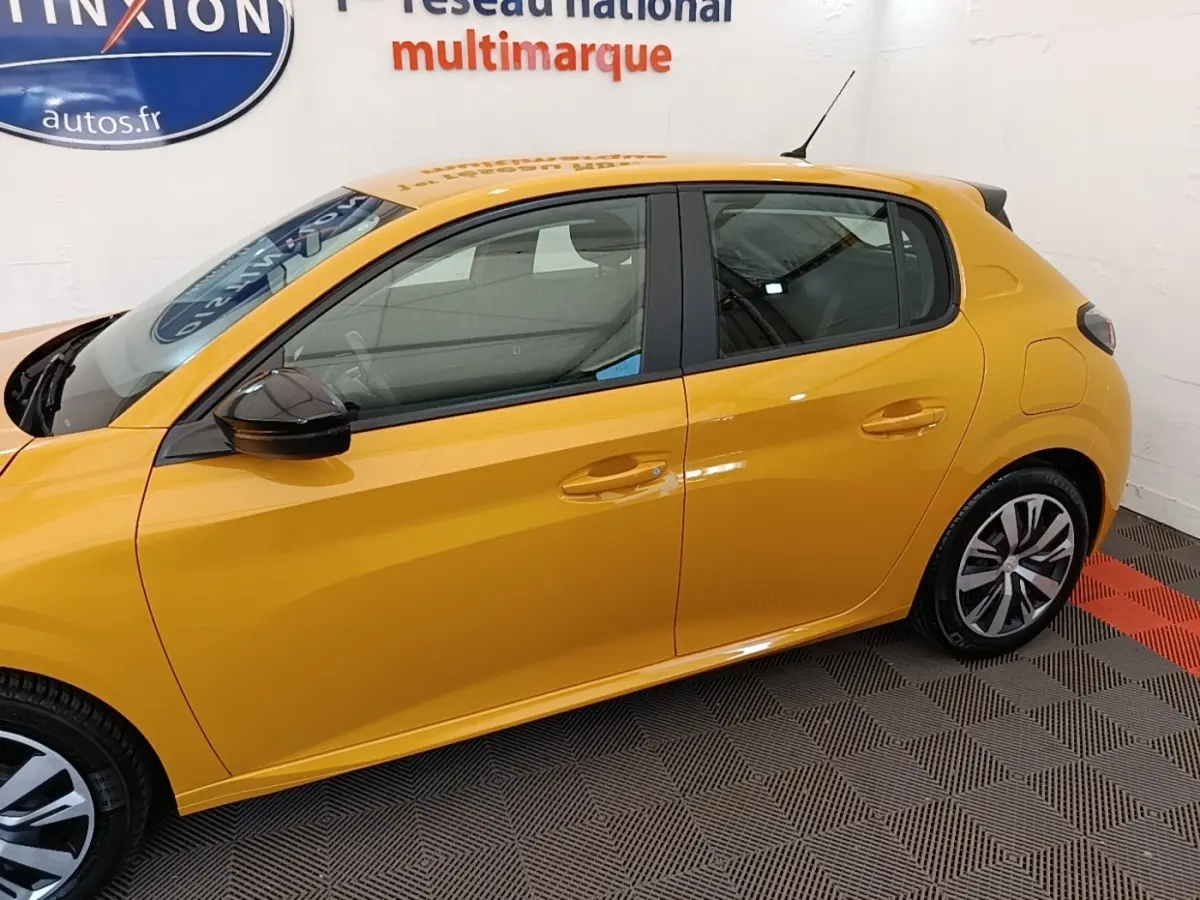 Profil droit d'une Peugeot 208 jaune 2023 avec rétroviseurs noirs et jantes bicolores dans un showroom.