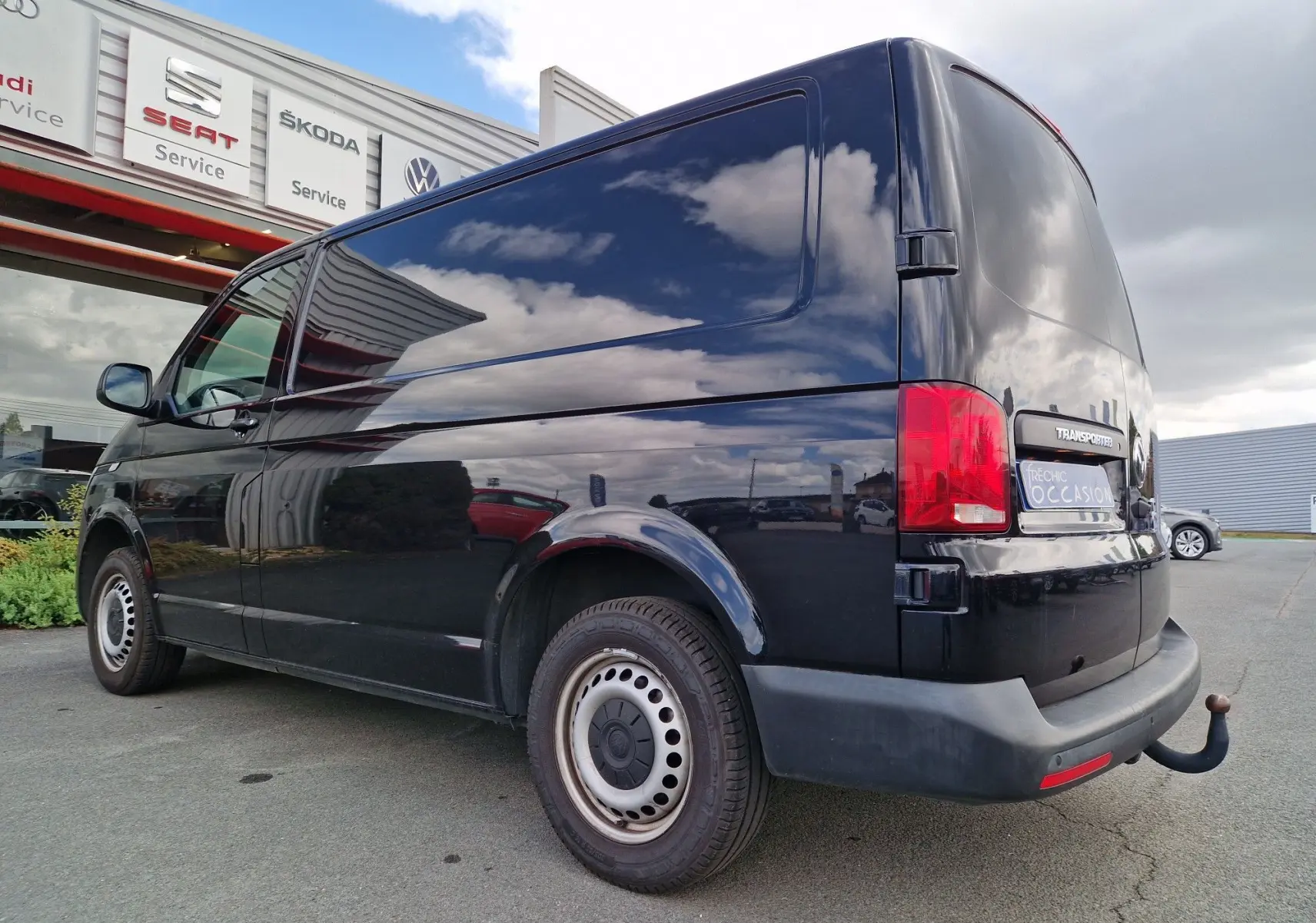 Vue 3/4 arrière droite d'un Volkswagen Transporter noir 2020 avec attelage rigide et feux arrière rouges.