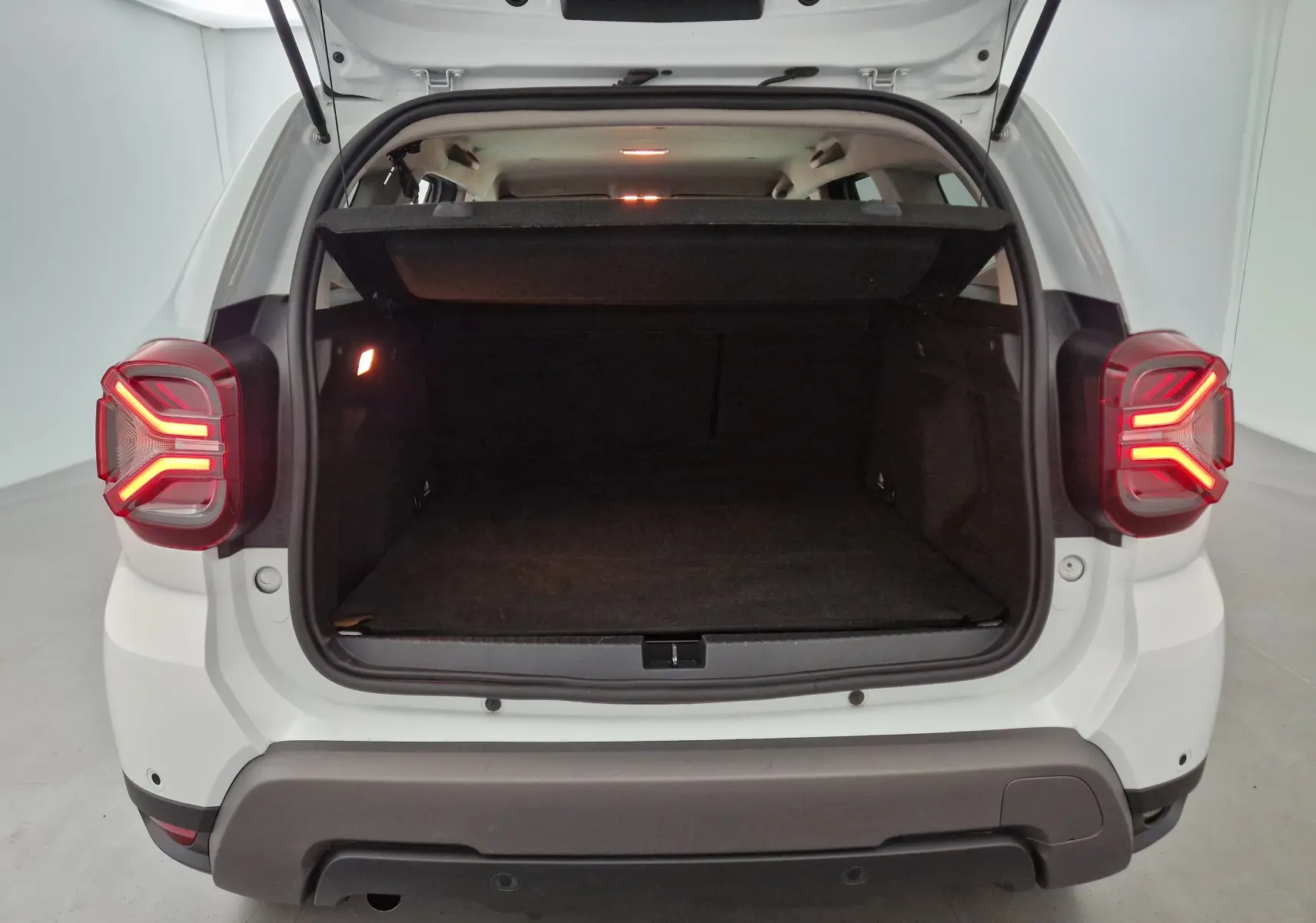 Coffre ouvert vu de l'arrière d'un Dacia Duster blanc 2024 avec feux arrière allumés et intérieur spacieux visible.