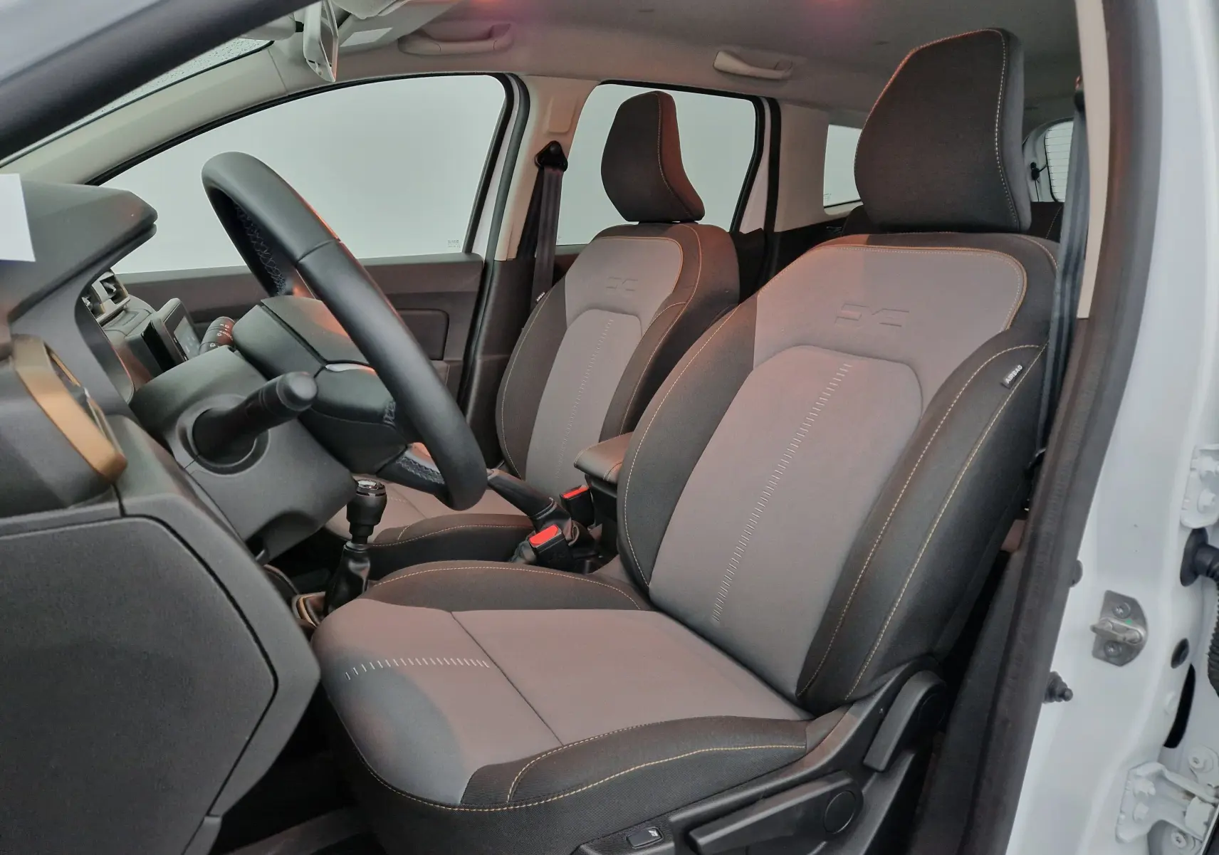 Vue intérieure côté gauche du Dacia Duster 4x4 blanc 2024, montrant les sièges avant gris avec surpiqûres contrastées.
