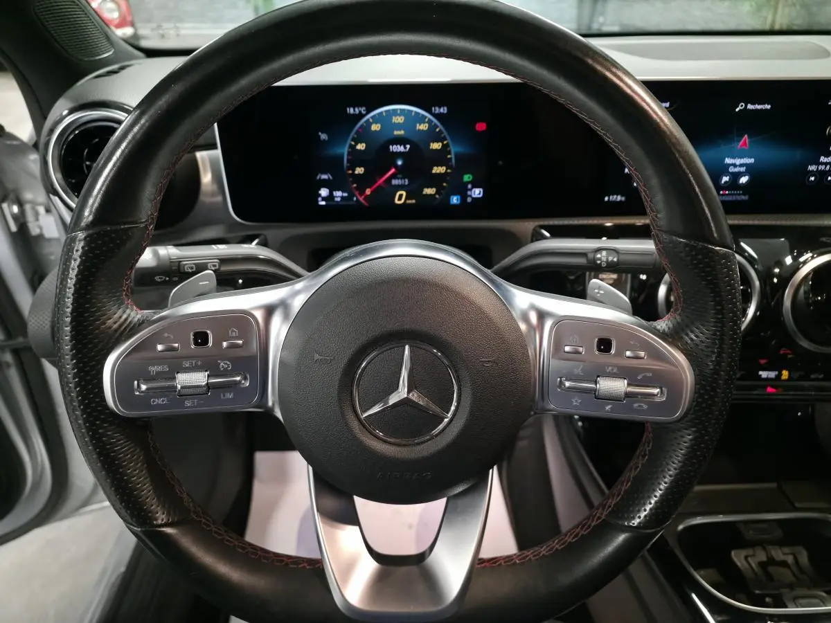 Vue rapprochée du volant sport cuir noir avec surpiqûres rouges et tableau de bord numérique de la Mercedes Classe A AMG Line 2019.