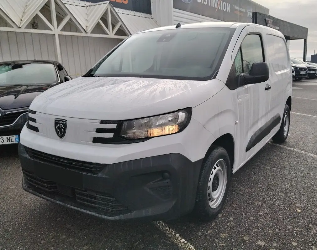 Peugeot Partner Fourgon blanc Icy vu en 3/4 avant droit, avec calandre noire et feux allumés.