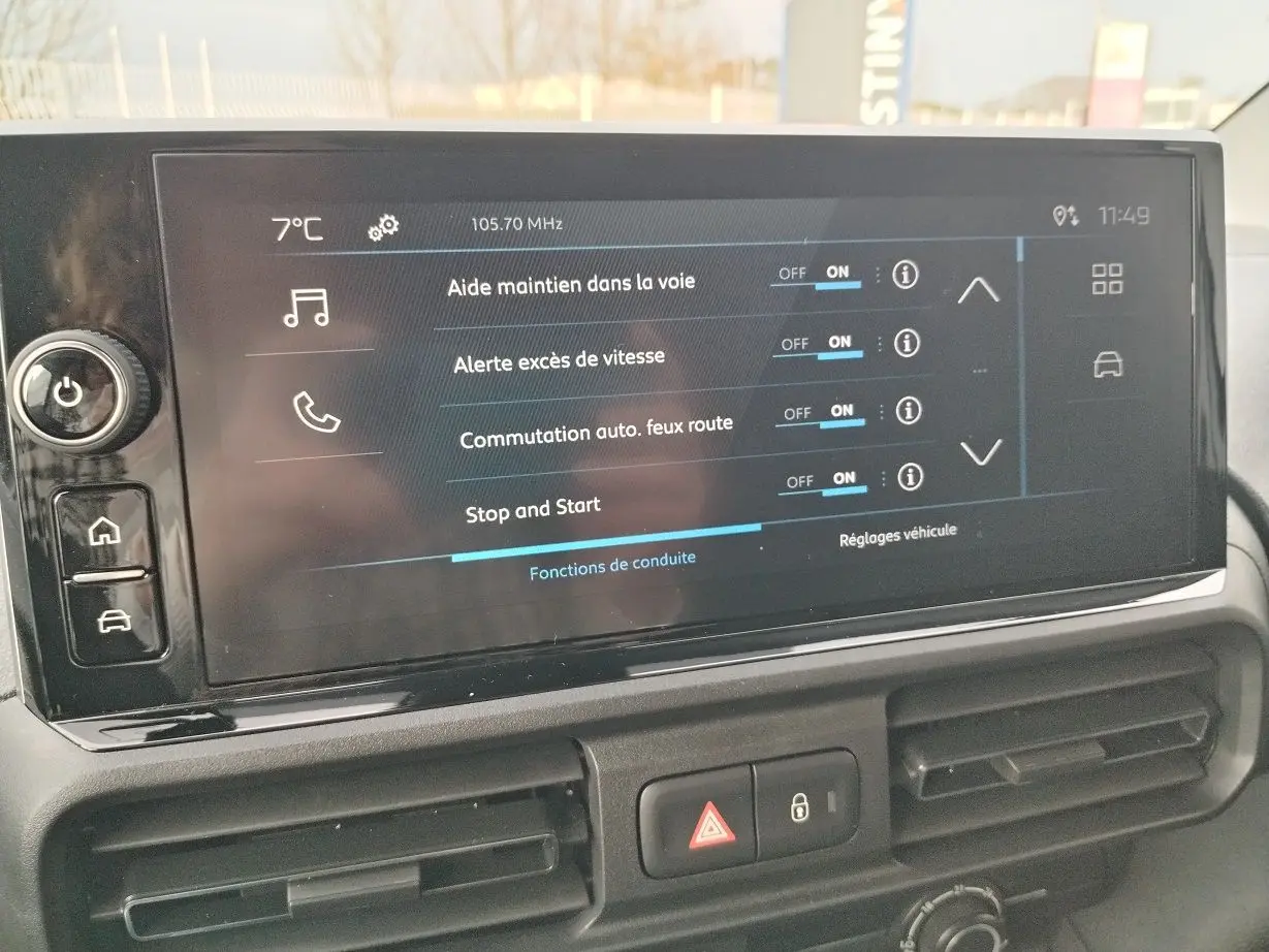 Vue intérieure centrée sur l'écran tactile du tableau de bord du Peugeot Partner Fourgon blanc Icy, affichant les aides à la conduite.