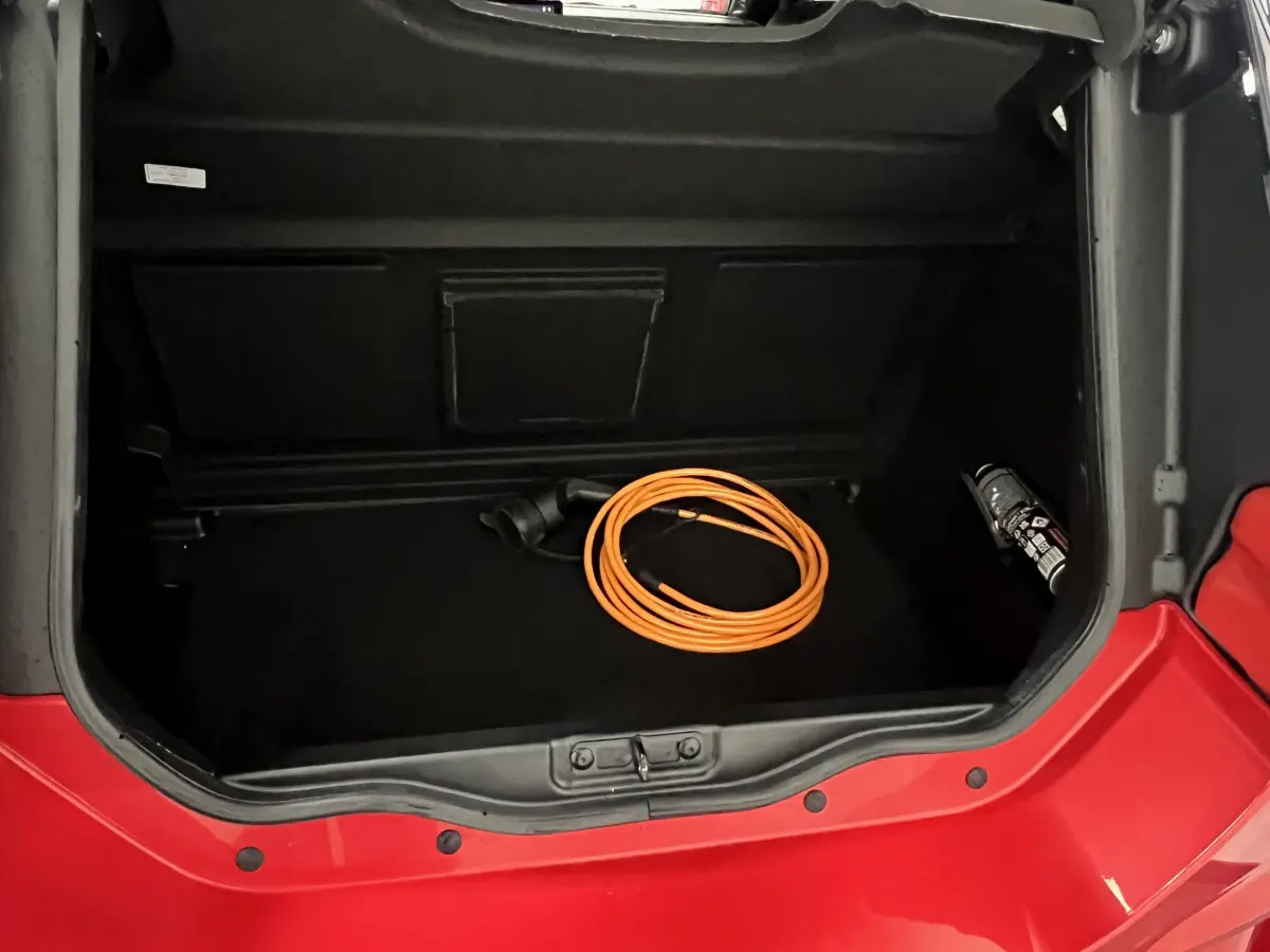Coffre ouvert vu de dessus du Ligier JS50 BEV 8KWH Elite rouge avec câble de charge électrique orange enroulé.