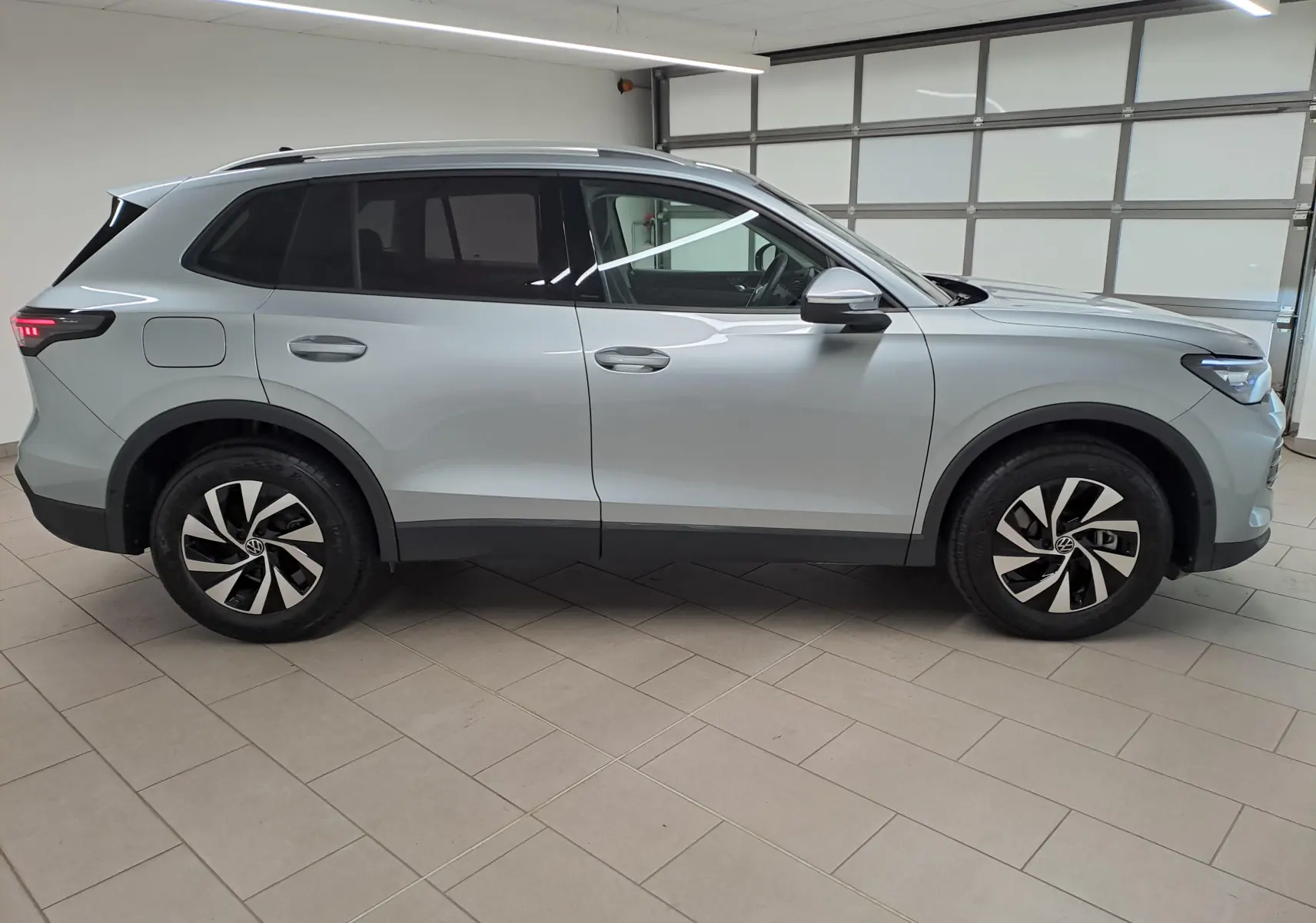 Vue de profil côté gauche d'un Volkswagen Tiguan 2025 argent Dolomite avec jantes noires et grises en intérieur showroom.
