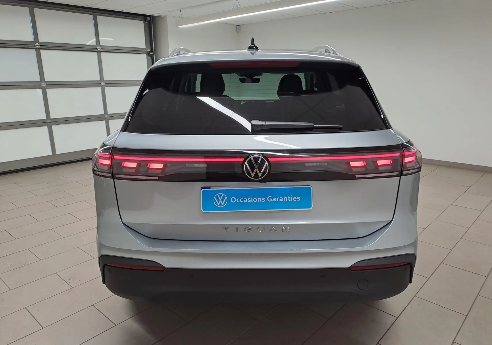 Vue arrière du Volkswagen Tiguan 2025 en Argent Dolomite avec feux arrière allumés et logo VW central.