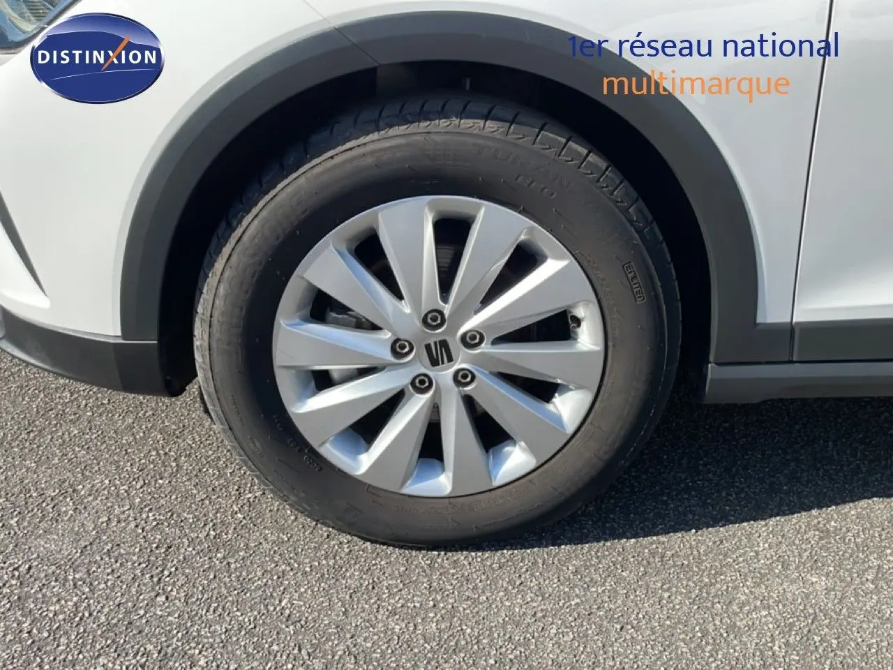 Gros plan sur la roue avant gauche d’un SEAT Arona blanc avec jante alliage grise et logo central visible.
