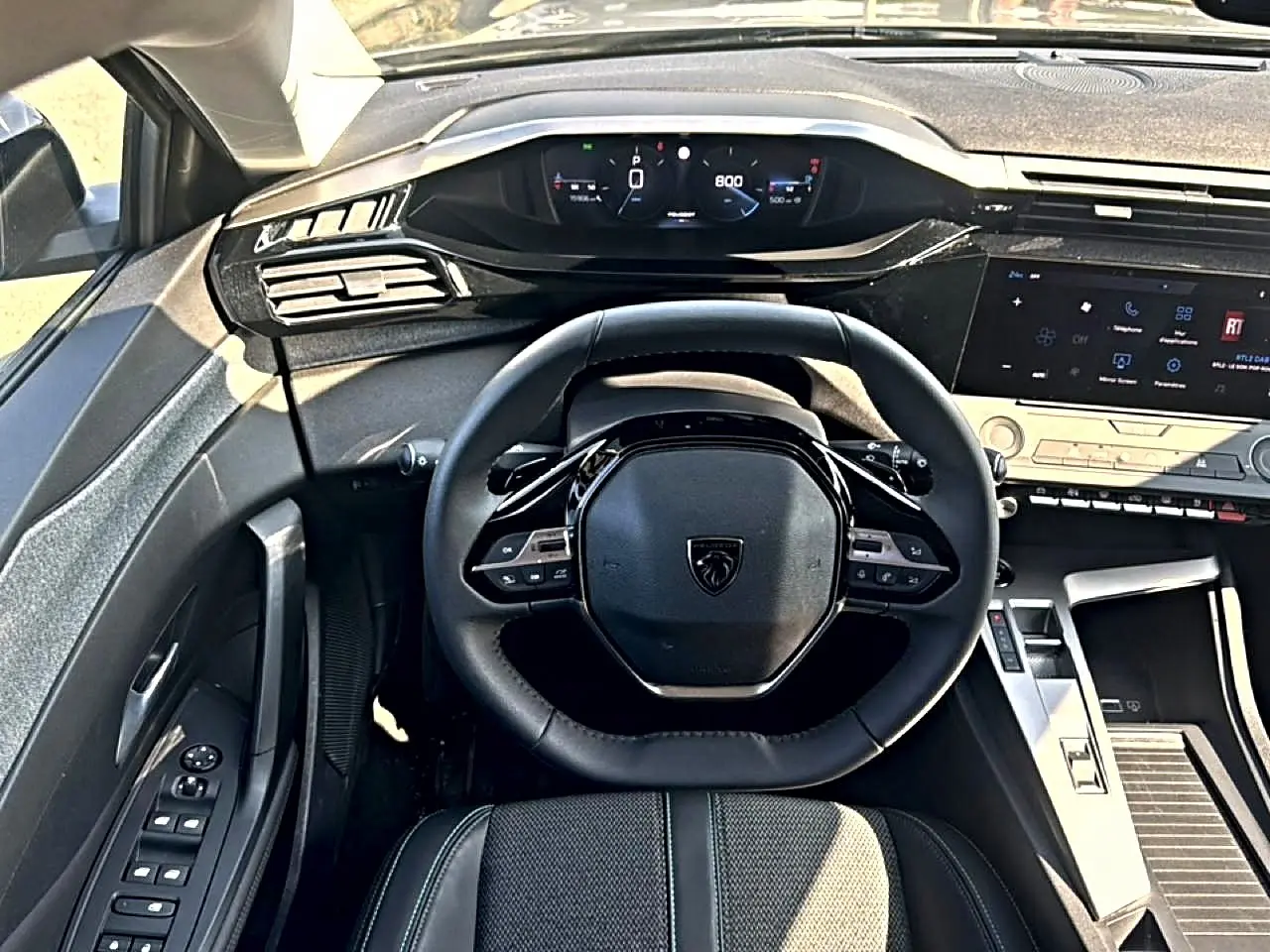 Vue intérieure centrée sur le volant noir et le tableau de bord numérique de la Peugeot 308 gris 2025.