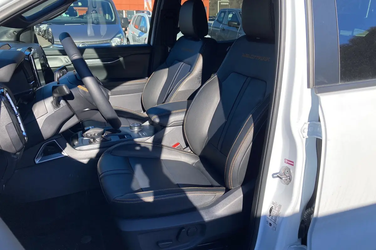 Vue intérieure côté conducteur du Ford Ranger blanc glacier 2026, sièges cuir noirs avec surpiqûres orange Wildtrak.