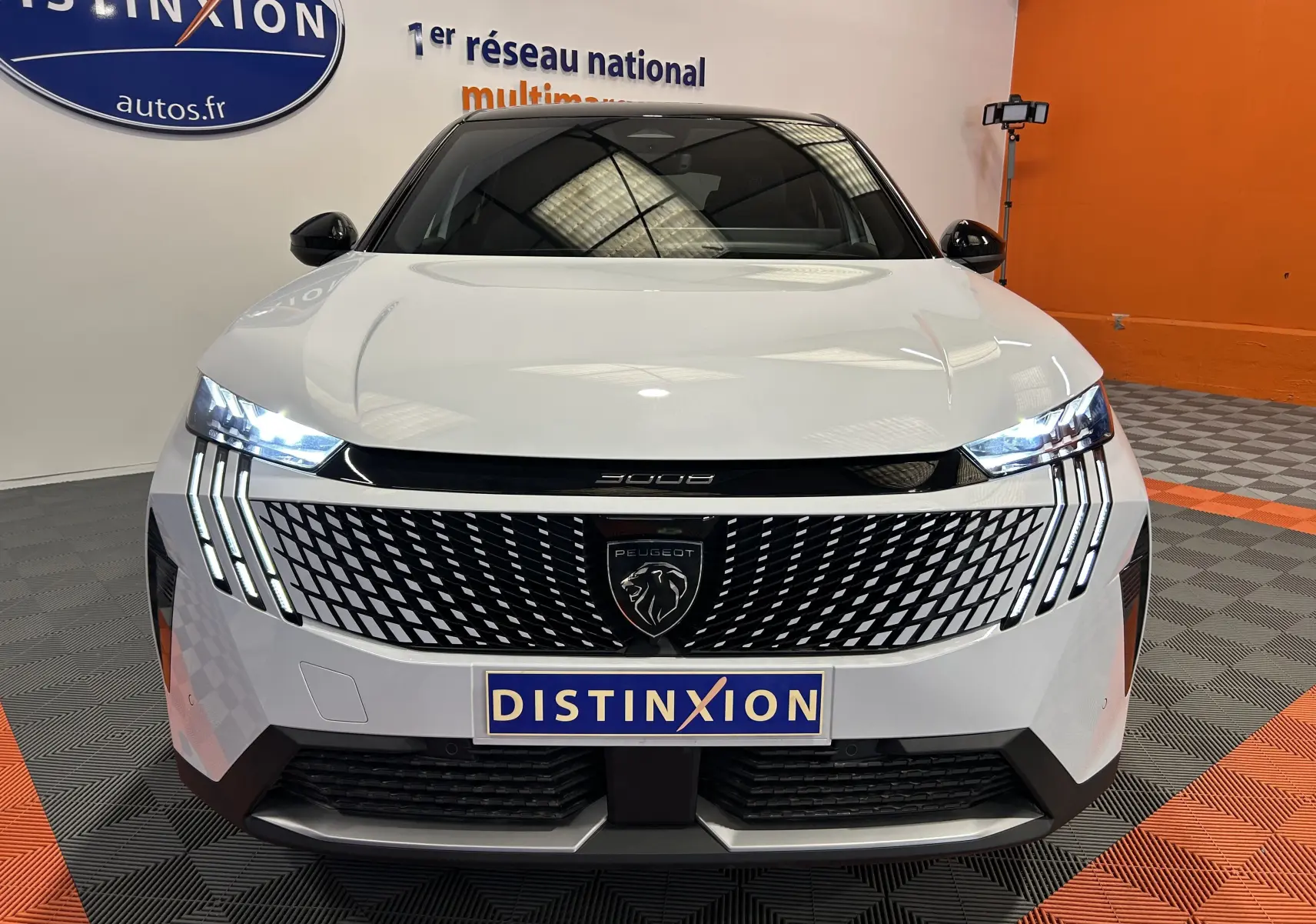 Vue frontale du Peugeot 3008 III Hybrid blanc Okenite avec calandre noire à motif géométrique et feux LED allumés.
