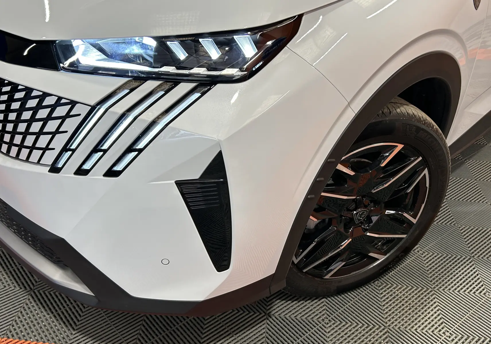 Gros plan sur l’avant droit blanc Okenite du Peugeot 3008 III Hybrid 145 GT avec phares LED et jante noire brillante.