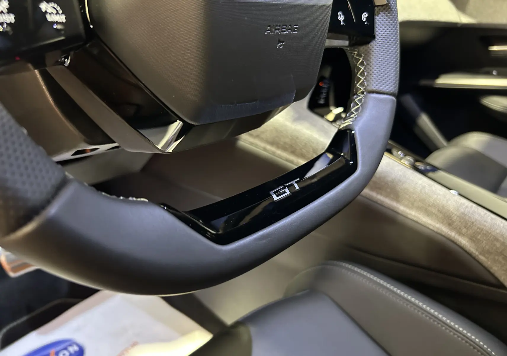 Gros plan sur le volant GT noir perforé du Peugeot 3008 hybride, avec intérieur cuir et détails modernes.