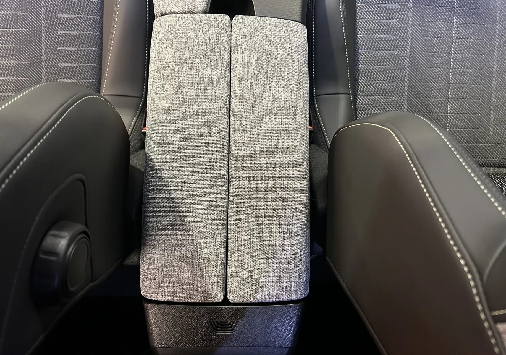Vue plongeante sur l'accoudoir central en tissu gris et les sièges avant en cuir noir avec surpiqûres blanches du Peugeot 3008 hybride 2025.