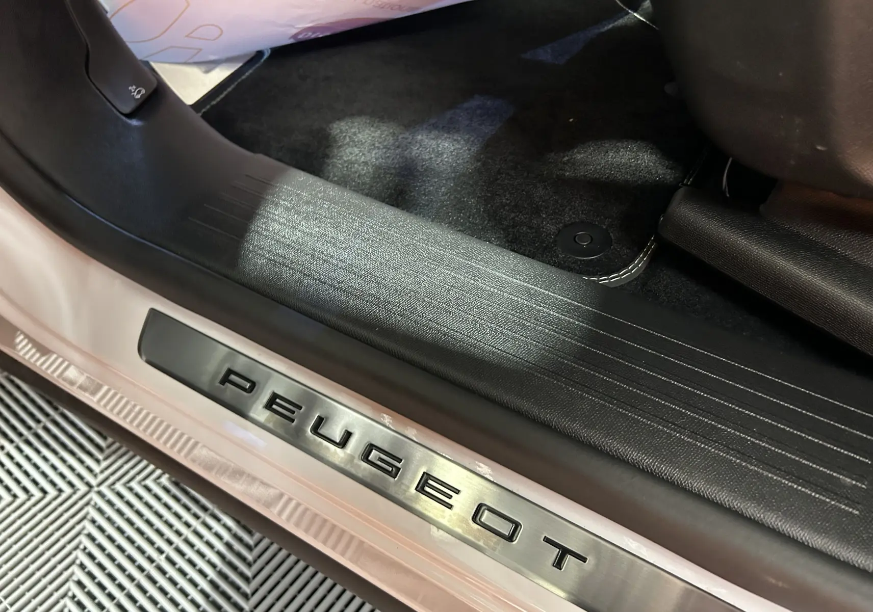 Gros plan sur la plaque de seuil de porte Peugeot avec intérieur noir et carrosserie blanc okenite visible.