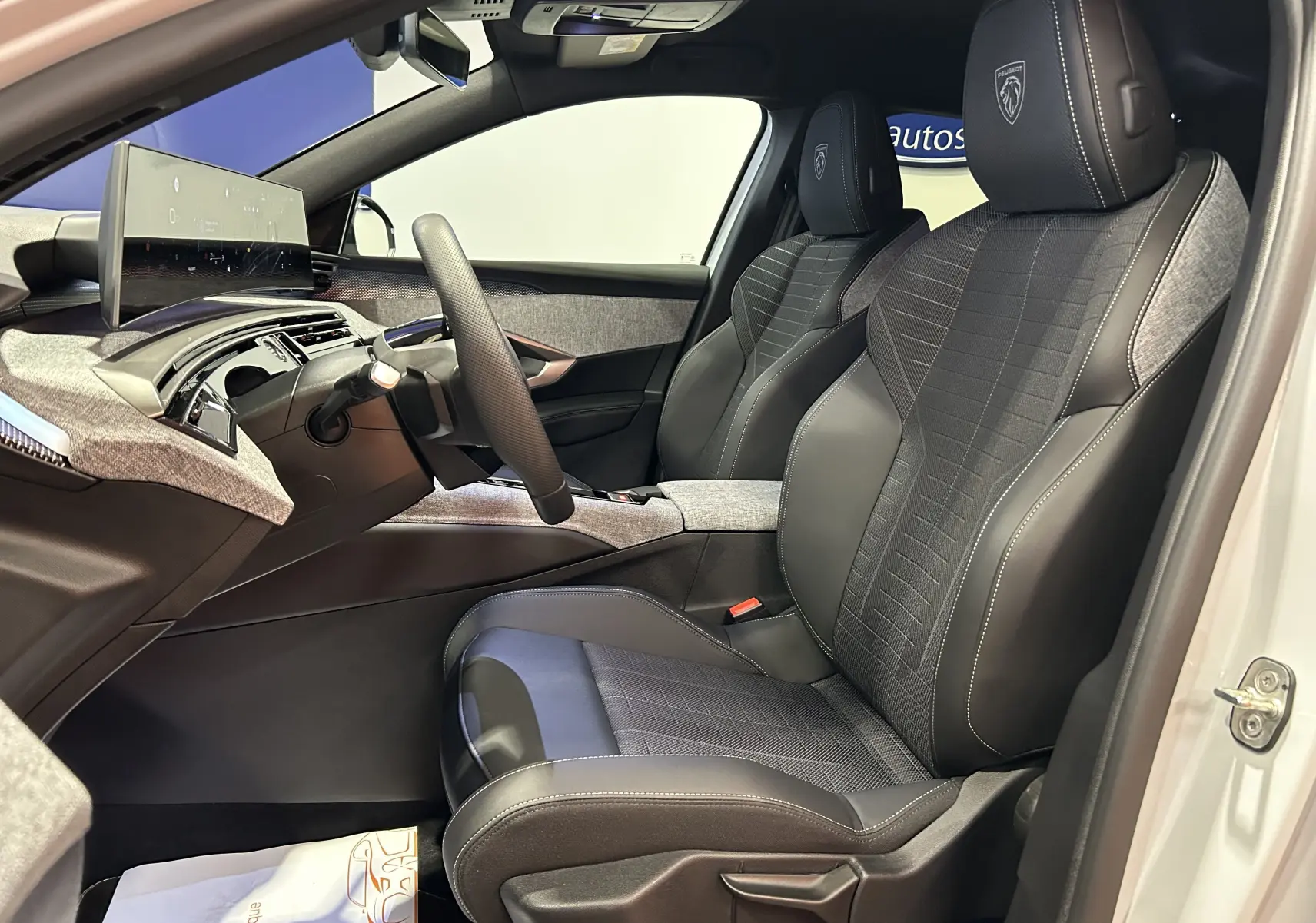 Vue intérieure côté conducteur du Peugeot 3008 III Hybrid 145, sièges noirs et gris avec logo Peugeot brodé.