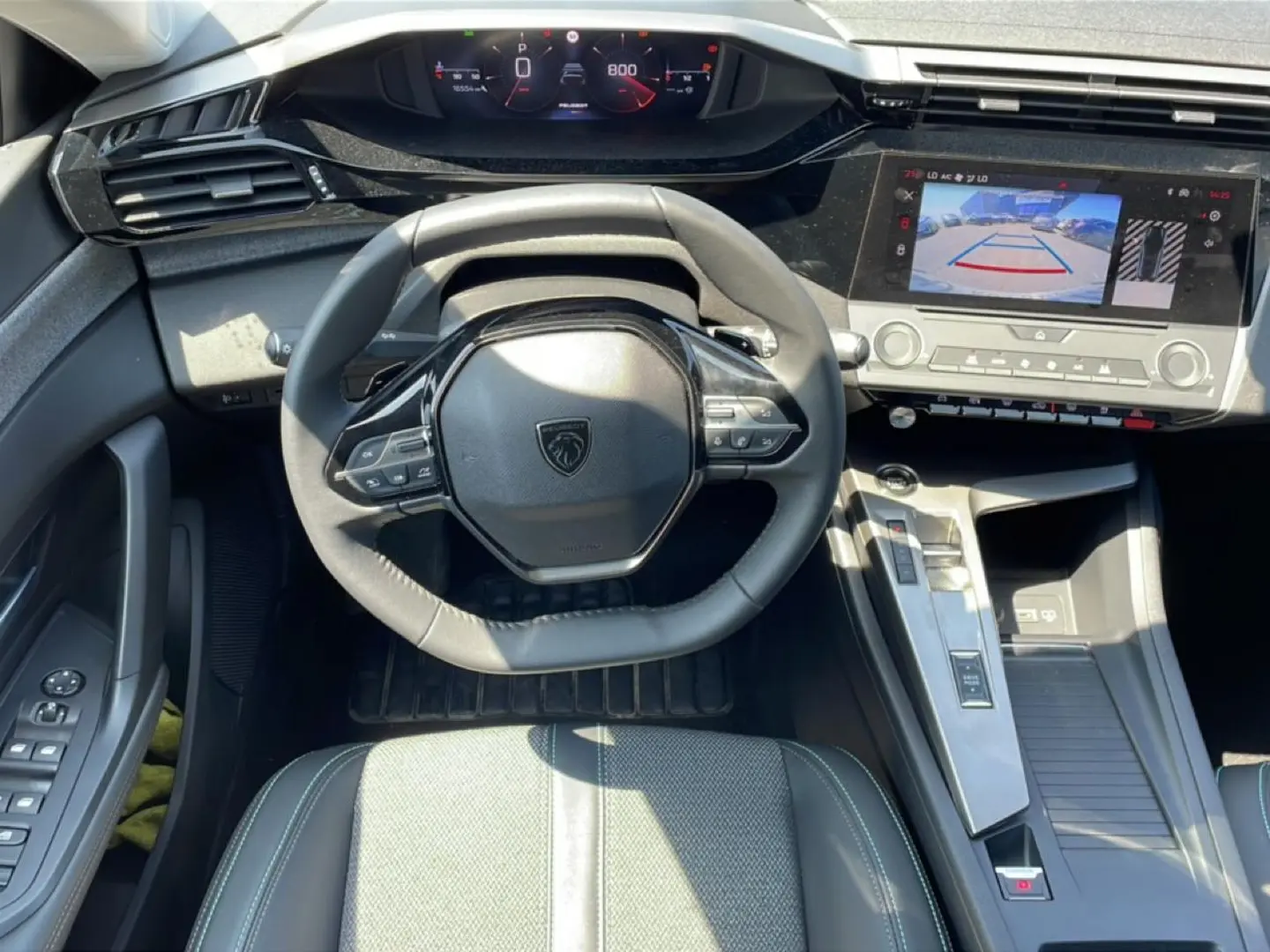 Vue intérieure avant centrée sur le volant cuir noir et l'écran tactile affichant la caméra de recul d'une Peugeot 308 gris 2025.