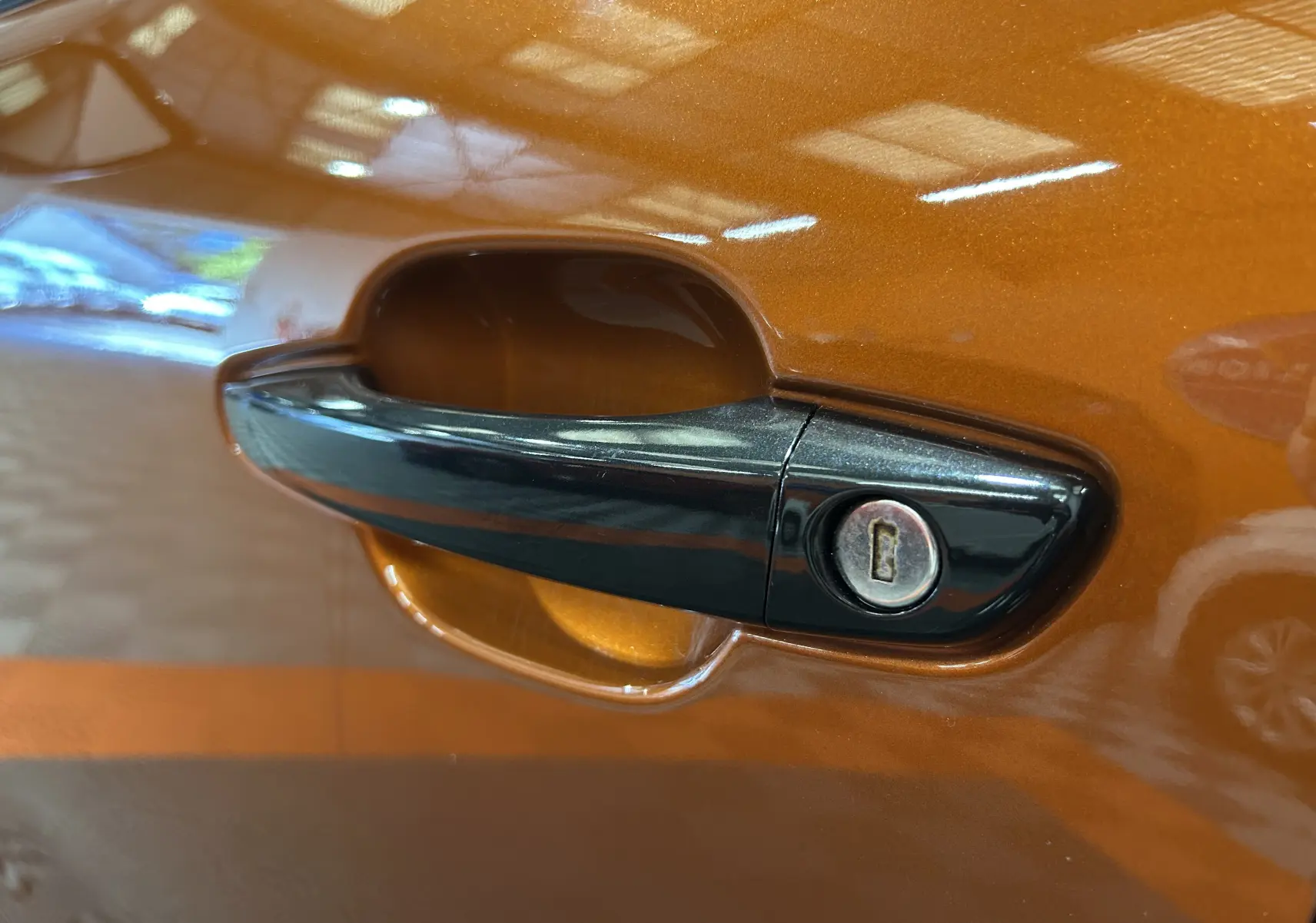 Poignée de porte noire en gros plan sur la portière orange métallisée d'une Citroën C4 PureTech 100 Feel 2021.