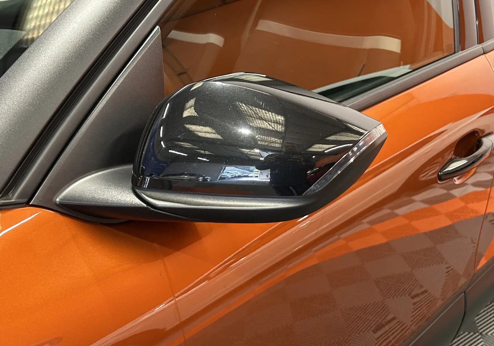 Rétroviseur noir en gros plan côté gauche sur une Citroën C4 PureTech 100 Feel orange 2021 avec caméra de recul.