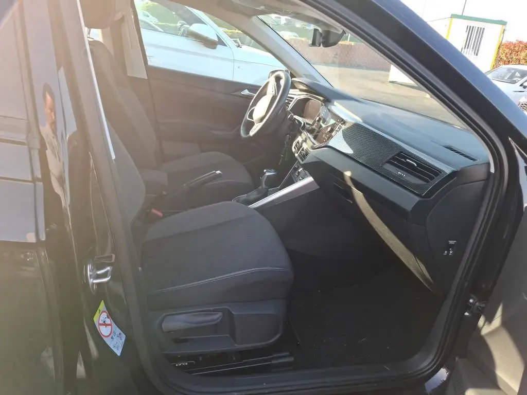Vue intérieure côté conducteur de la Volkswagen Polo noire 2022, montrant sièges tissu et tableau de bord moderne.