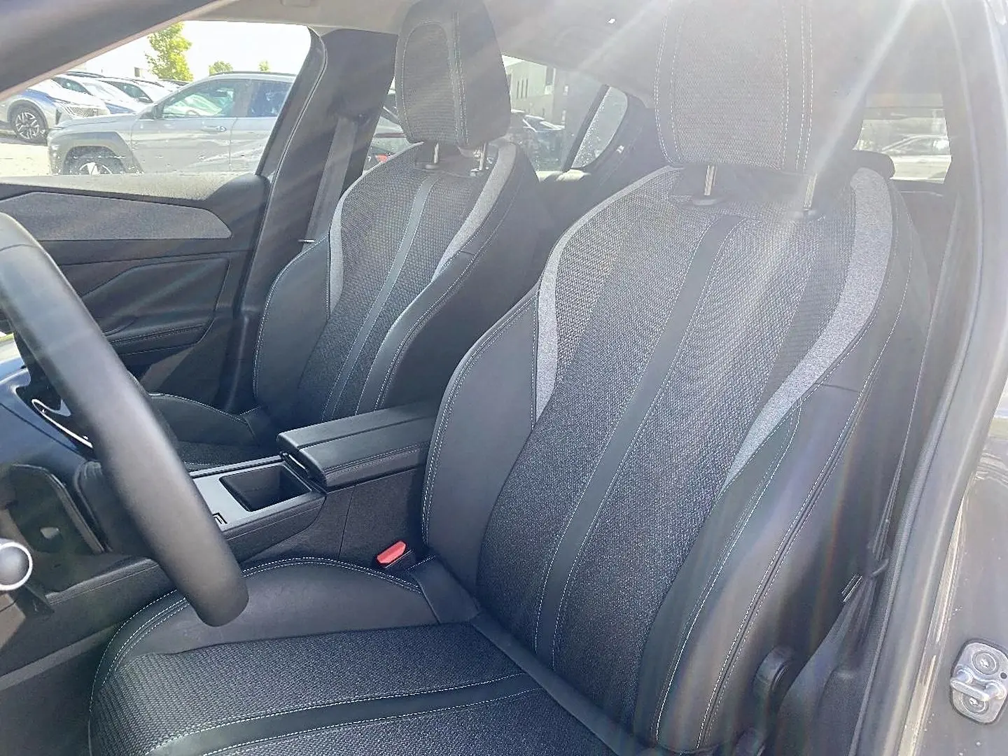Intérieur de la Peugeot 308 2025, vue sur les sièges avant en tissu gris avec surpiqûres blanches et accoudoir central.