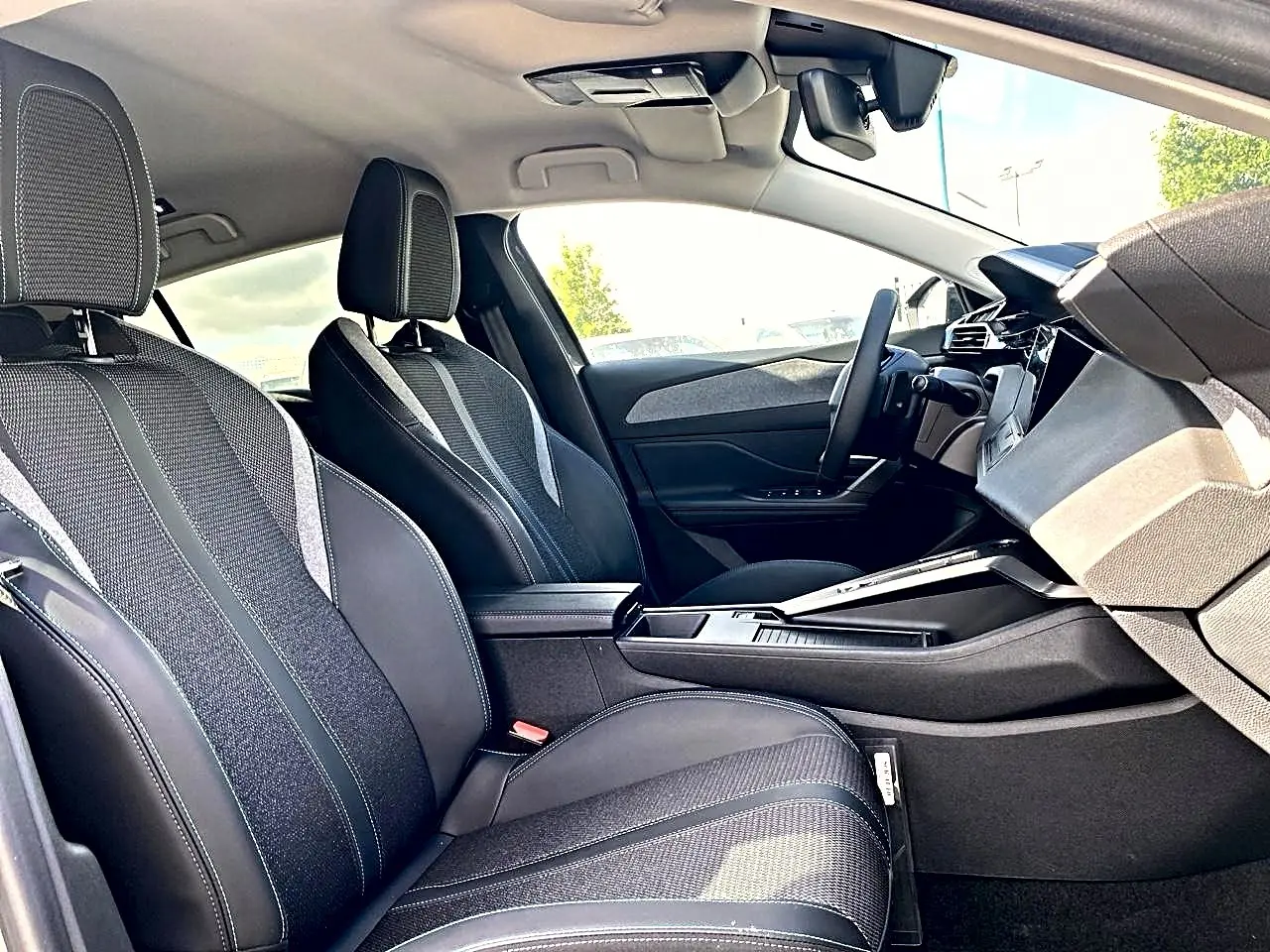 Vue intérieure côté droit de la Peugeot 308 2025, sièges tissu noir avec surpiqûres et console centrale moderne.