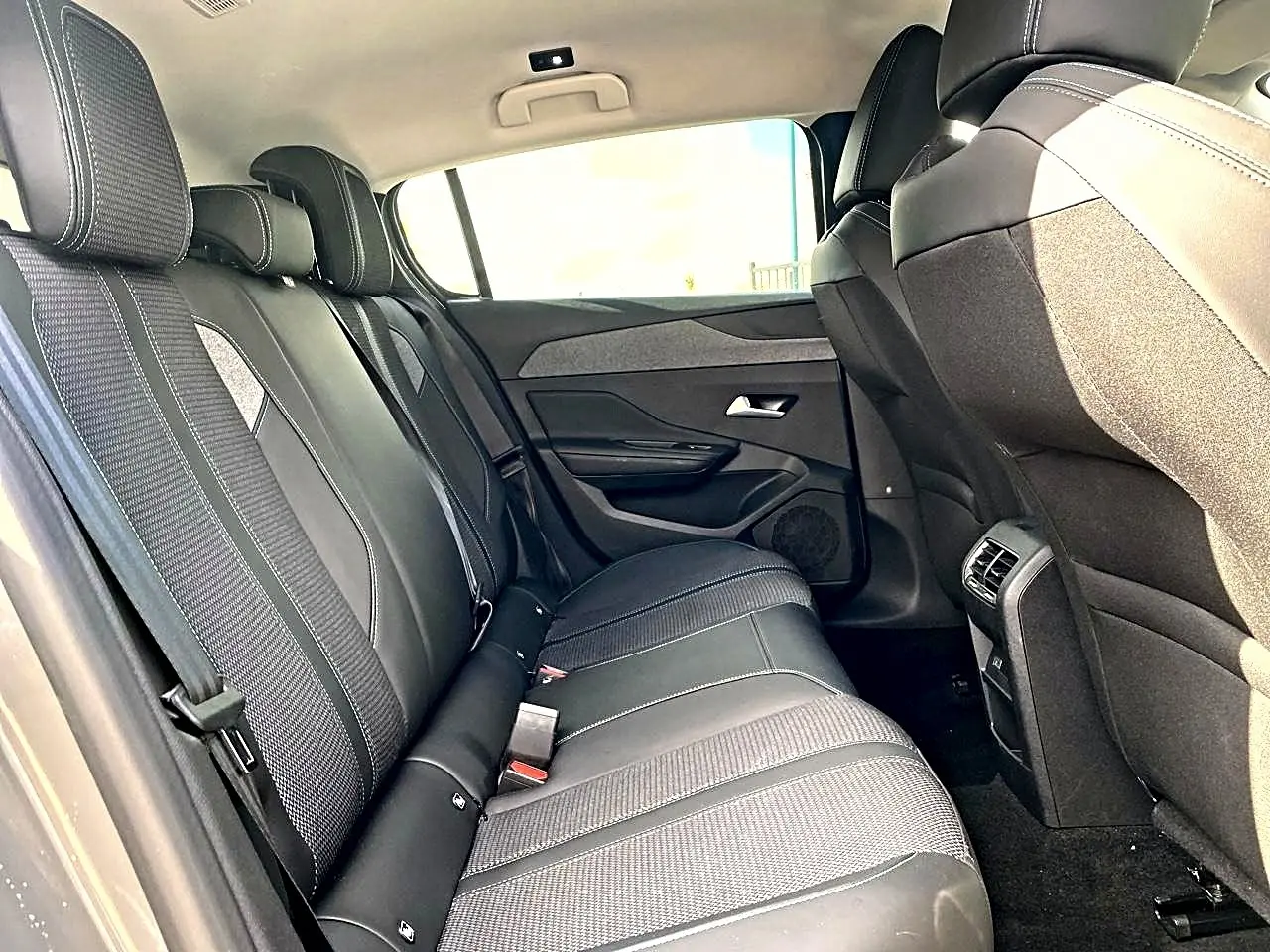 Vue intérieure côté droit montrant la banquette arrière noire avec surpiqûres blanches et les dossiers avant du Peugeot 308 gris.