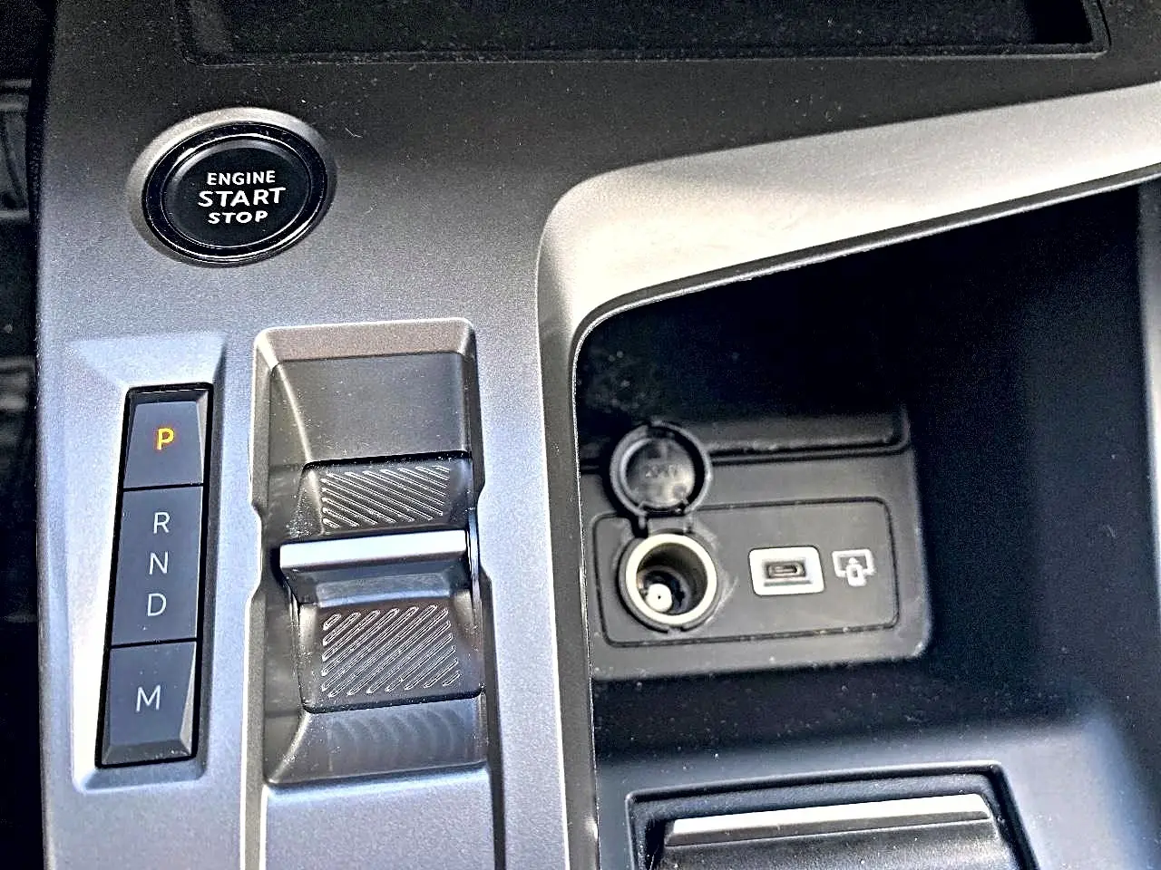 Gros plan sur la console centrale grise de la Peugeot 308 2025 montrant la commande de boîte auto et prise USB avec allume-cigare.
