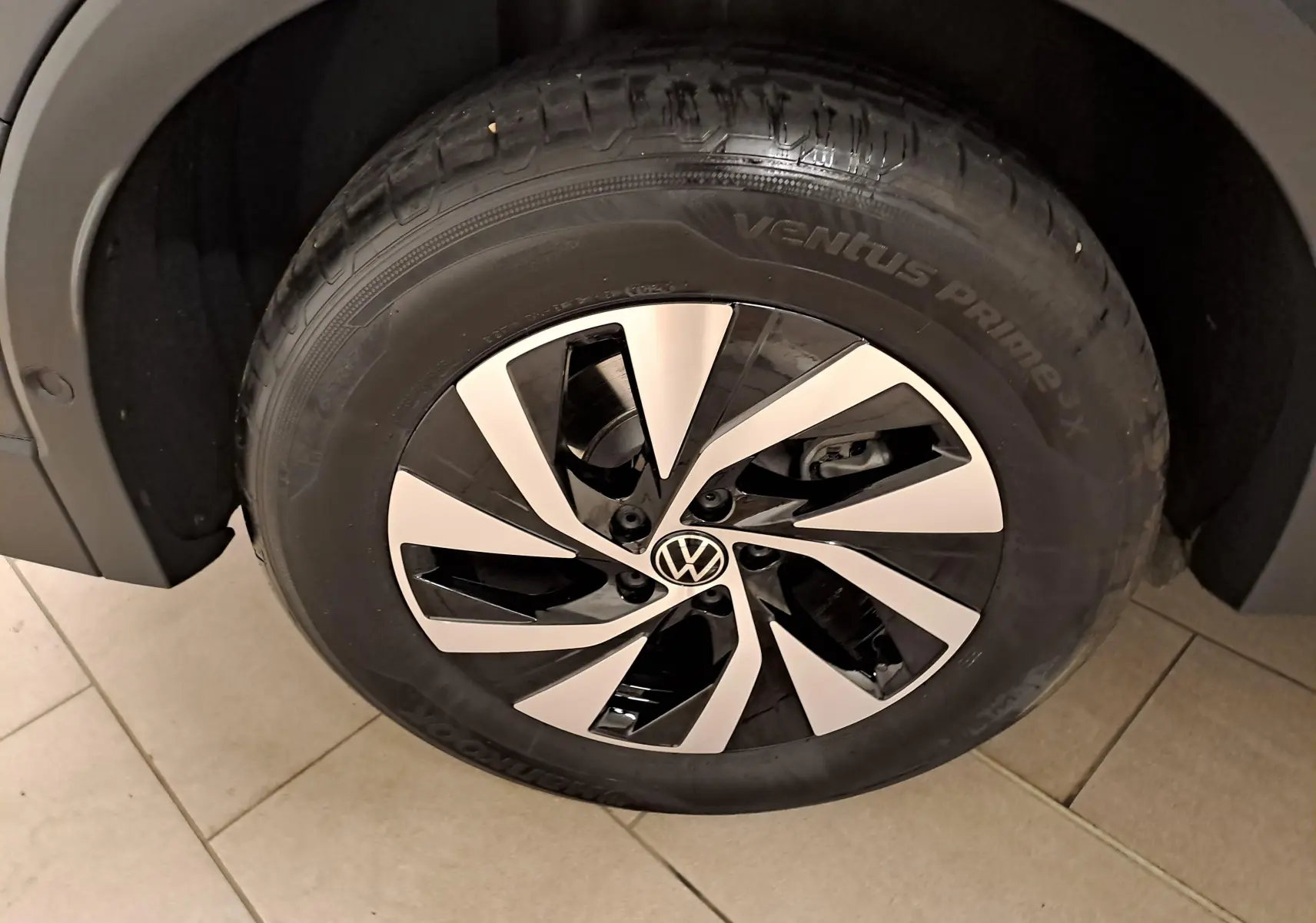 Gros plan sur la roue avant gauche du Volkswagen Tiguan 2024 Gris Urano avec jante alliage bicolore et logo VW central.