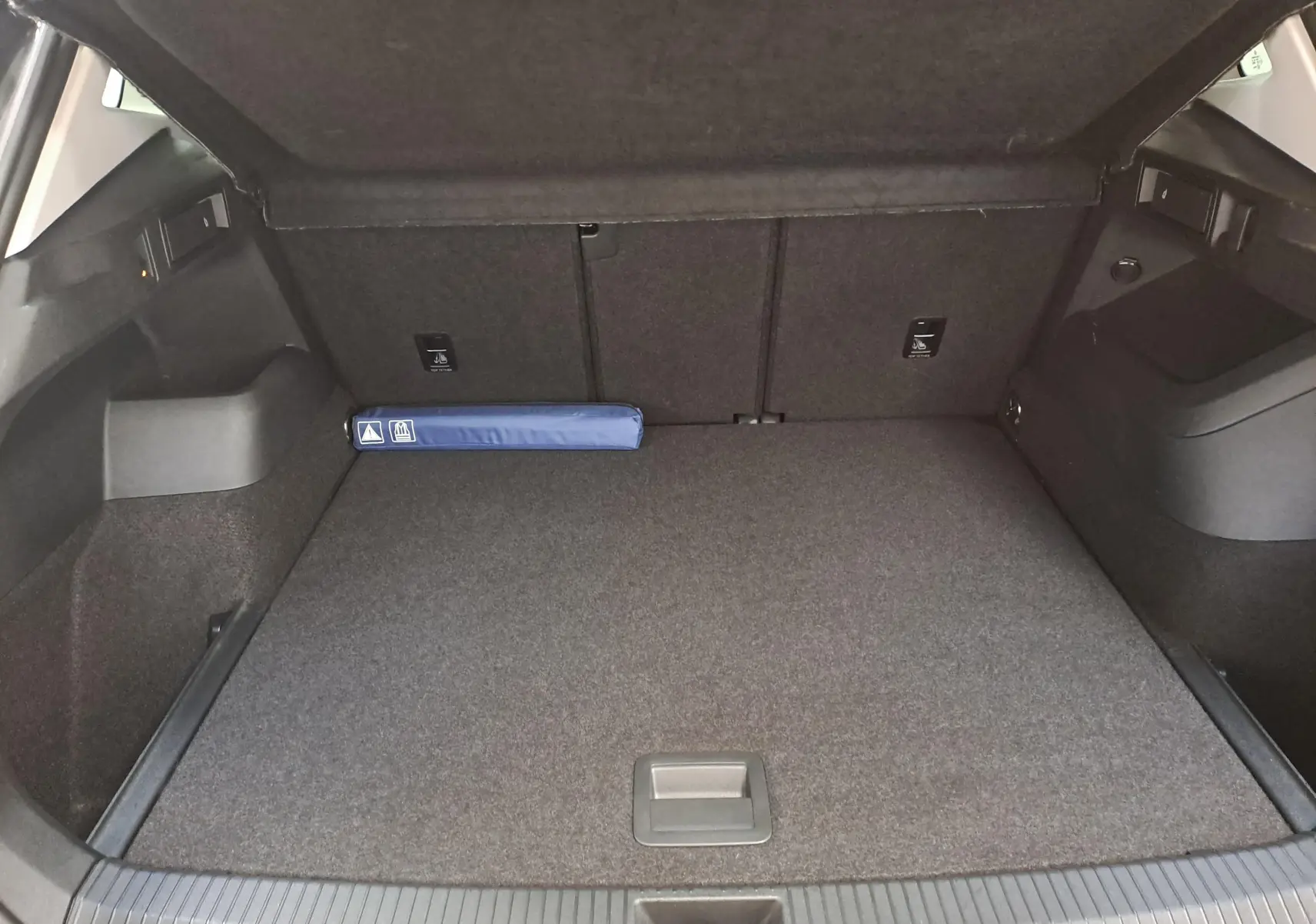 Coffre ouvert du Volkswagen Tiguan 2024 gris Urano, vue intérieure montrant un espace de rangement plat et un kit de sécurité bleu.