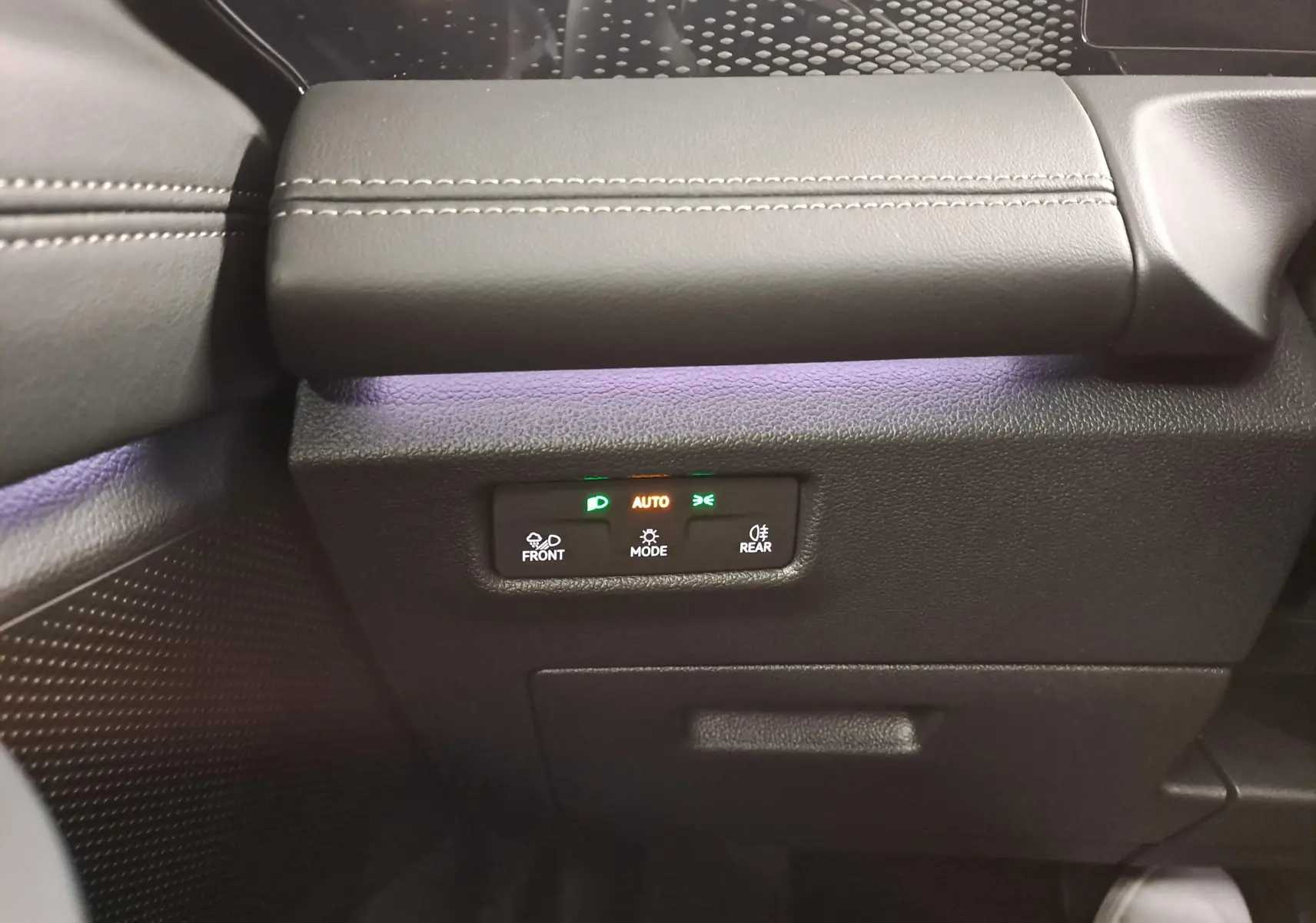 Gros plan sur le panneau de commandes des feux avec éclairage ambiant violet dans l'habitacle gris du Volkswagen Tiguan 2024.