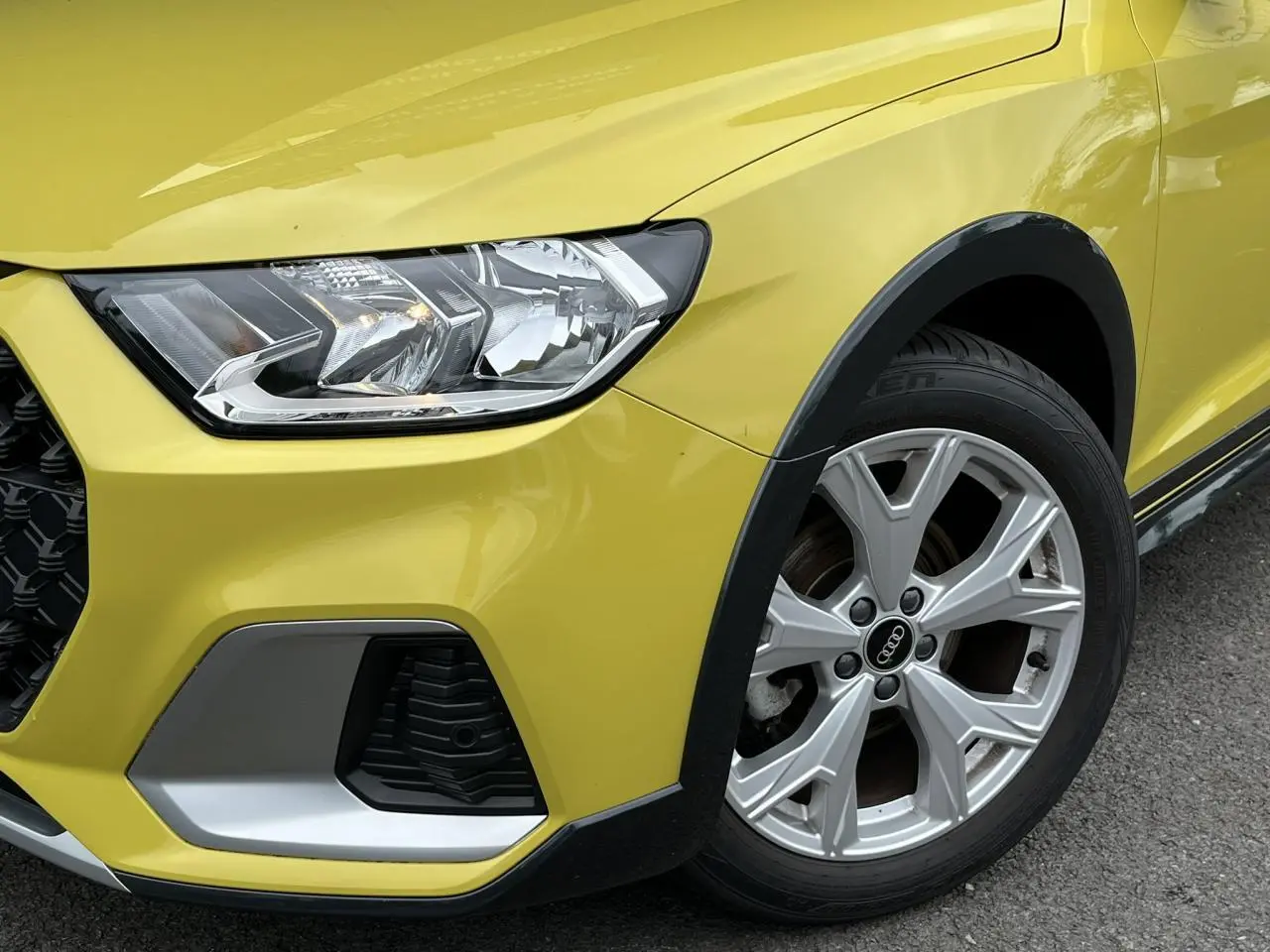 Gros plan sur l'avant droit d'une Audi A1 Allstreet jaune Python, mettant en valeur le phare et la jante en aluminium.