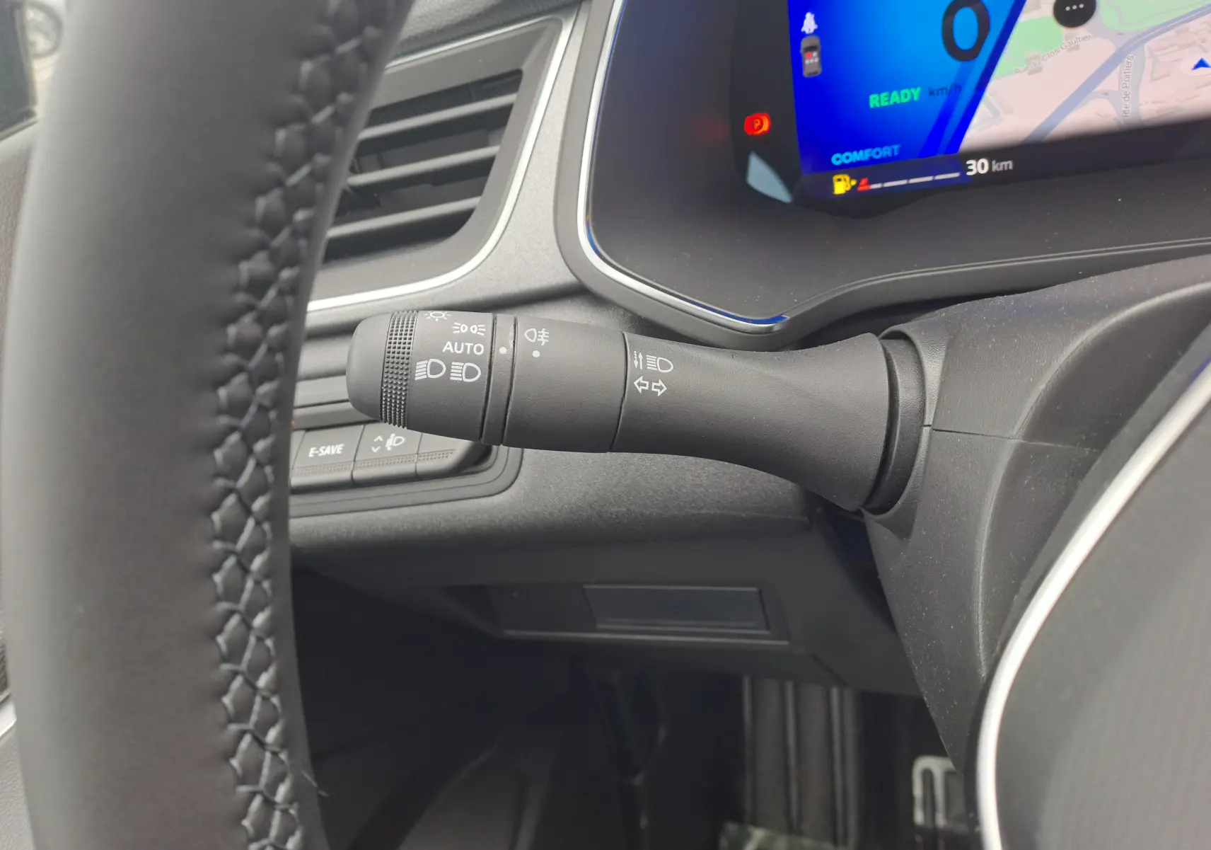 Gros plan sur la commande des phares à gauche du volant dans l'habitacle gris du Renault Symbioz 2024.