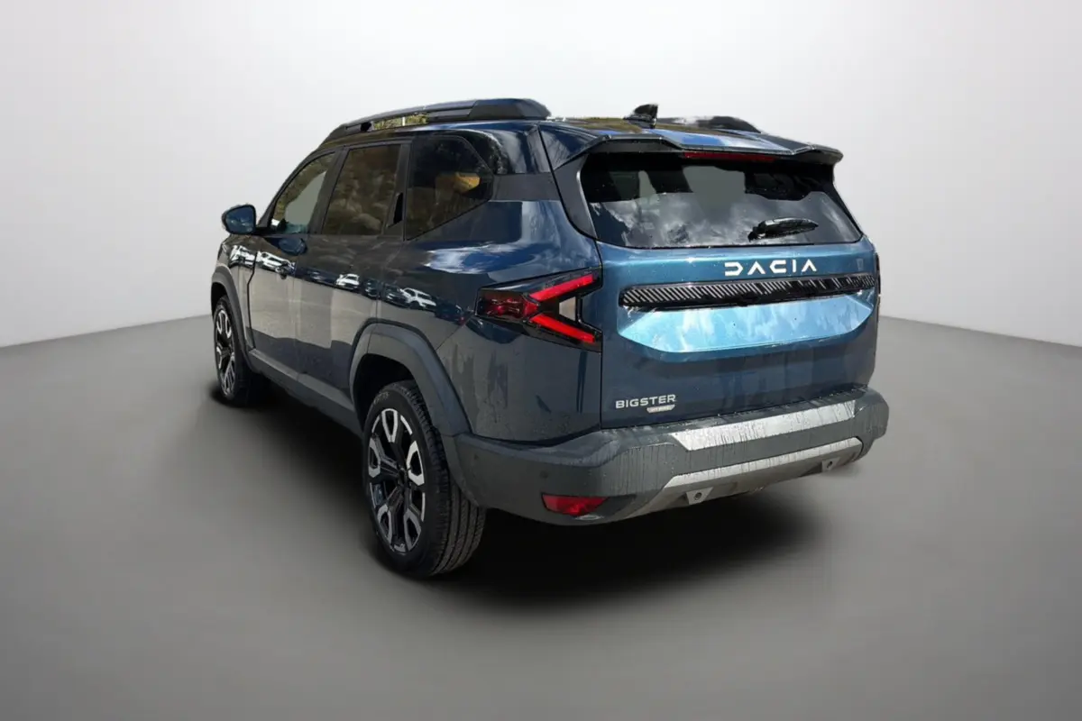 Vue 3/4 arrière gauche d'un Dacia Bigster bleu indigo avec toit noir et jantes alu 19 pouces dans un studio.