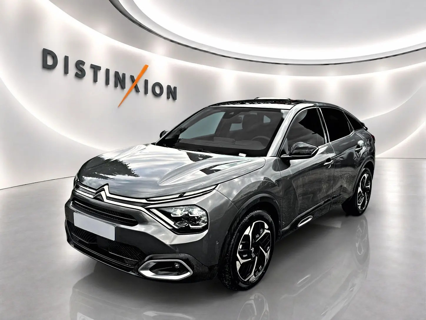 Citroën C4 gris 3/4 avant droit, avec jantes noires et toit panoramique en showroom lumineux.
