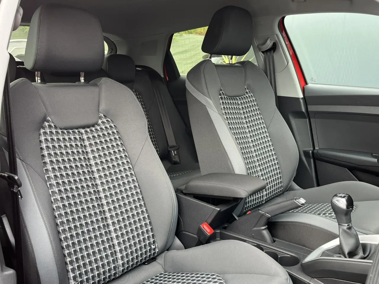 Vue intérieure des sièges avant gris à motifs géométriques de l'Audi A1 Sportback rouge Misano, avec accoudoir central.