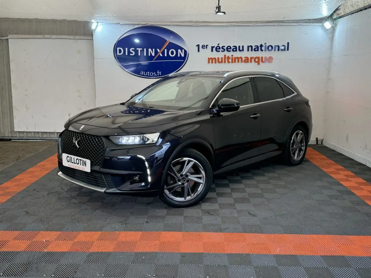 DS7 Crossback E-TENSE bleu en 3/4 avant droit, avec calandre distinctive et feux LED allumés dans un showroom.