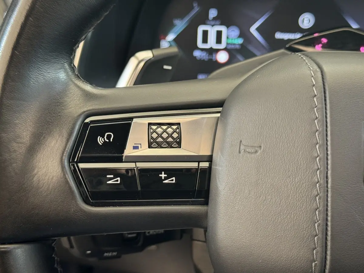 Gros plan sur les commandes gauche du volant cuir noir du DS7 Crossback E-TENSE 4x4, avec tableau de bord numérique en arrière-plan.