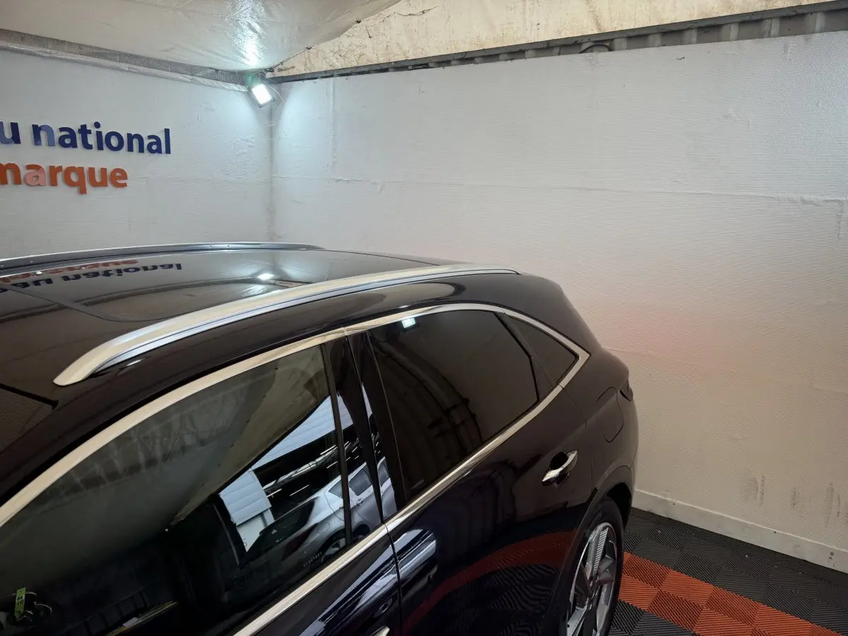 Vue latérale droite du DS7 Crossback bleu avec barres de toit chromées et vitres teintées dans un garage.