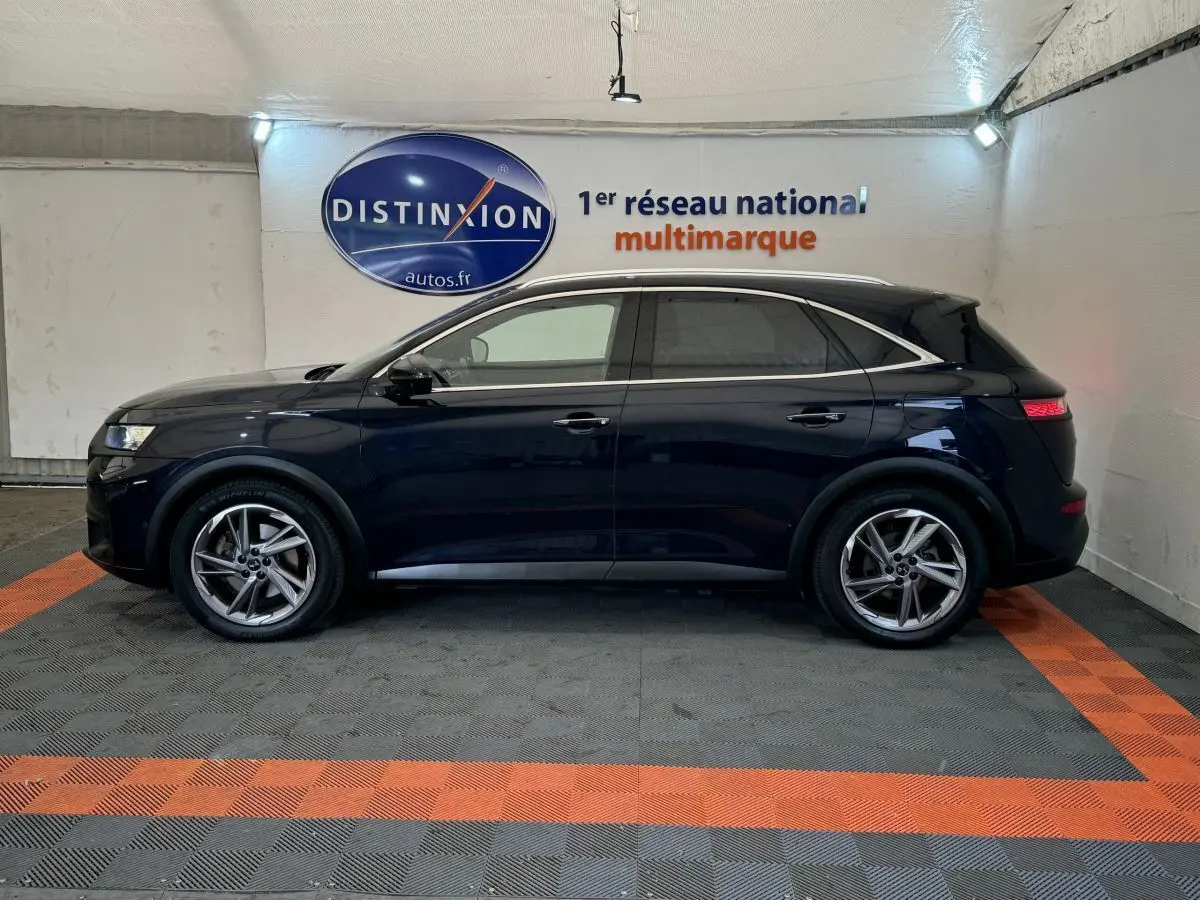 Vue latérale droite d'un DS7 Crossback E-TENSE bleu avec toit noir, dans un showroom au sol gris et orange.