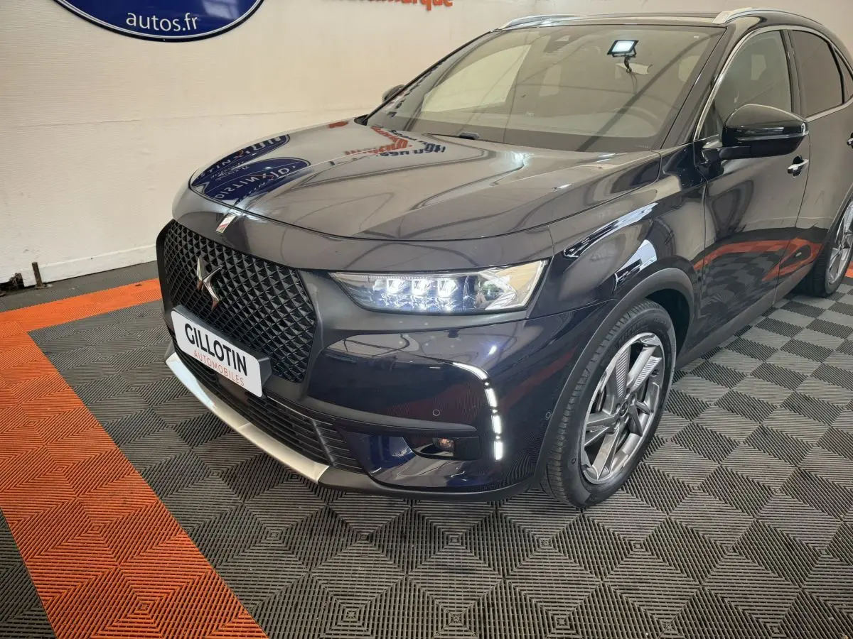 Vue 3/4 avant droit du DS7 Crossback E-TENSE bleu avec calandre noire et feux LED allumés en intérieur showroom.