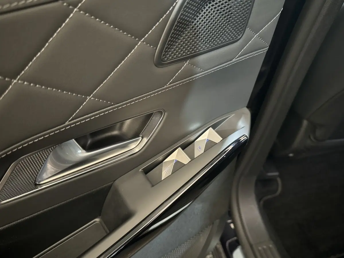 Gros plan sur la porte intérieure côté gauche du DS7 Crossback bleu, avec commandes de vitres et surpiqûres apparentes.