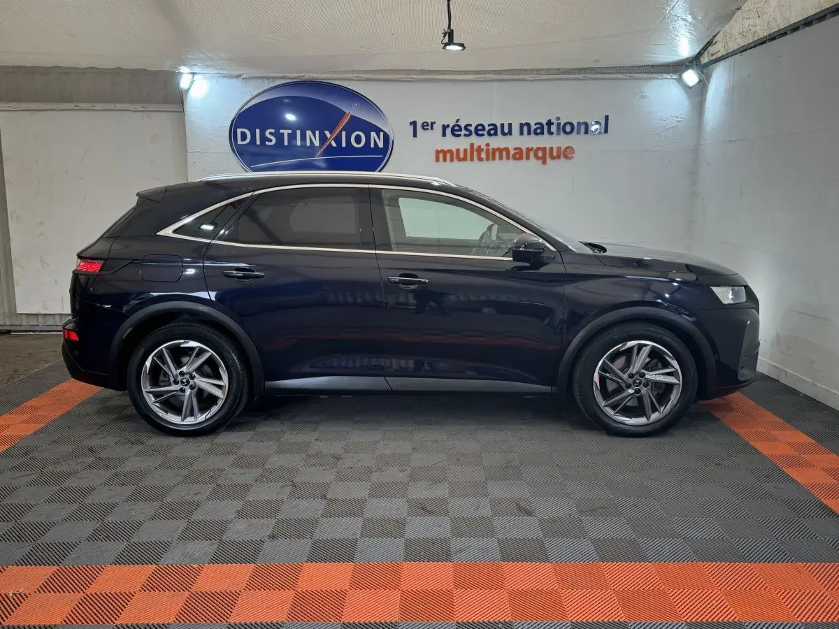 Vue latérale droite d'un DS7 Crossback E-TENSE bleu foncé dans un showroom avec sol gris et orange.