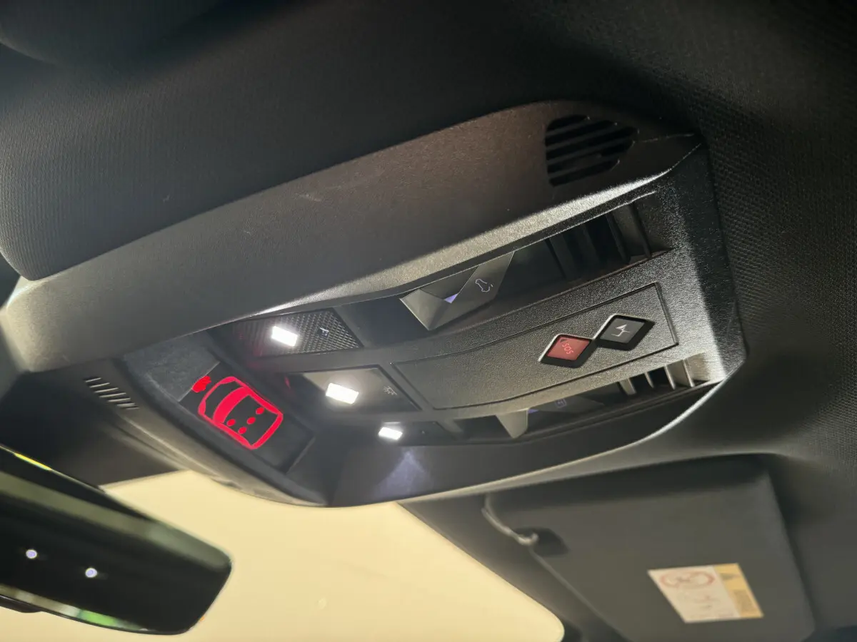 Vue en contre-plongée du panneau de commandes au plafond du DS7 Crossback bleu, avec éclairage et boutons SOS visibles.