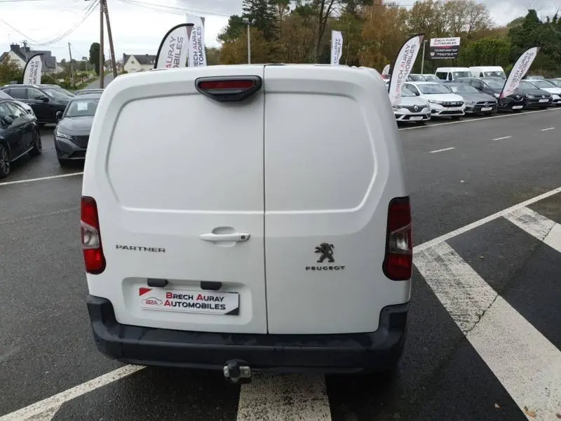 Vue arrière d'un utilitaire blanc Peugeot Partner avec portes battantes et attelage visible sur parking.