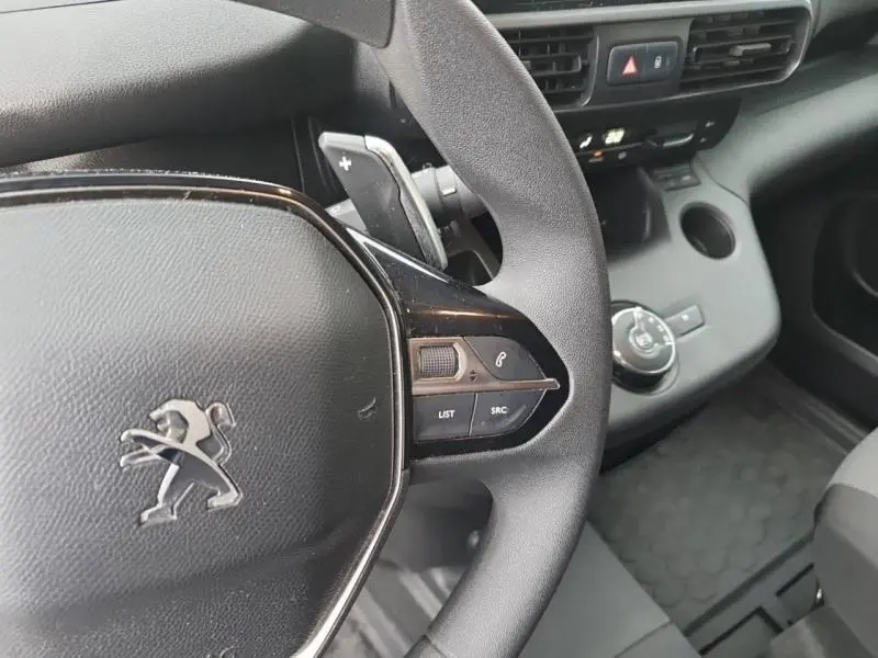 Gros plan sur le volant noir multifonction du Peugeot Partner blanc, avec commandes vocales et tableau de bord partiel visible.