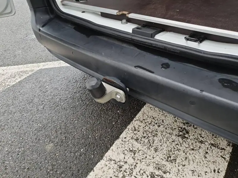 Gros plan sur le crochet d'attelage arrière du Peugeot Partner blanc, avec plancher bois visible dans le coffre ouvert.
